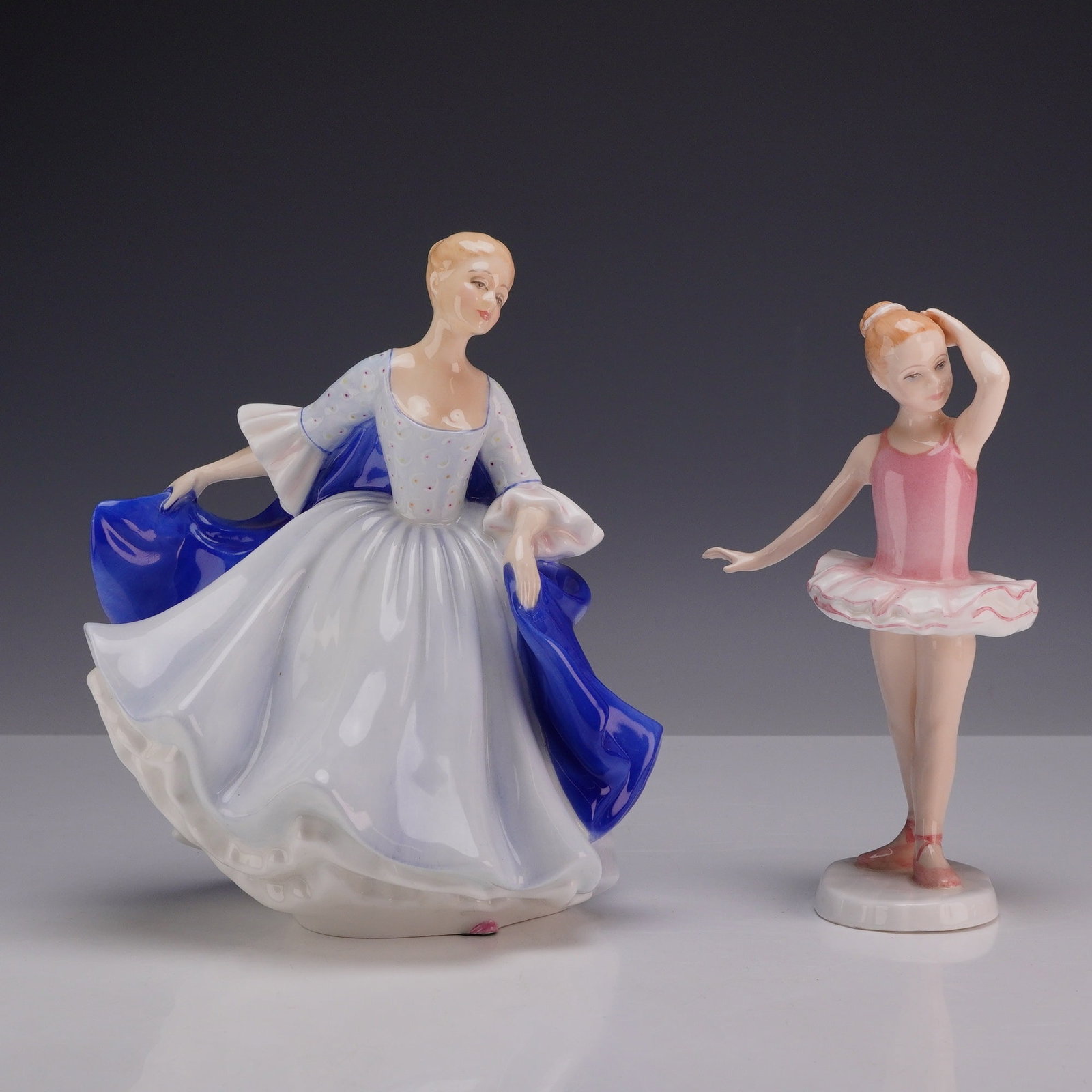 2pc Royal Doulton Bone China Figurines, Dulcie HN2305 and Little Ballerina HN3431: This collection features two Royal Doulton porcelain figures. "Dulcie," designed by Peggy Davies, portrays an elegant woman dressed in a flowing pale blue gown accented with a dark blue cape. Also inc