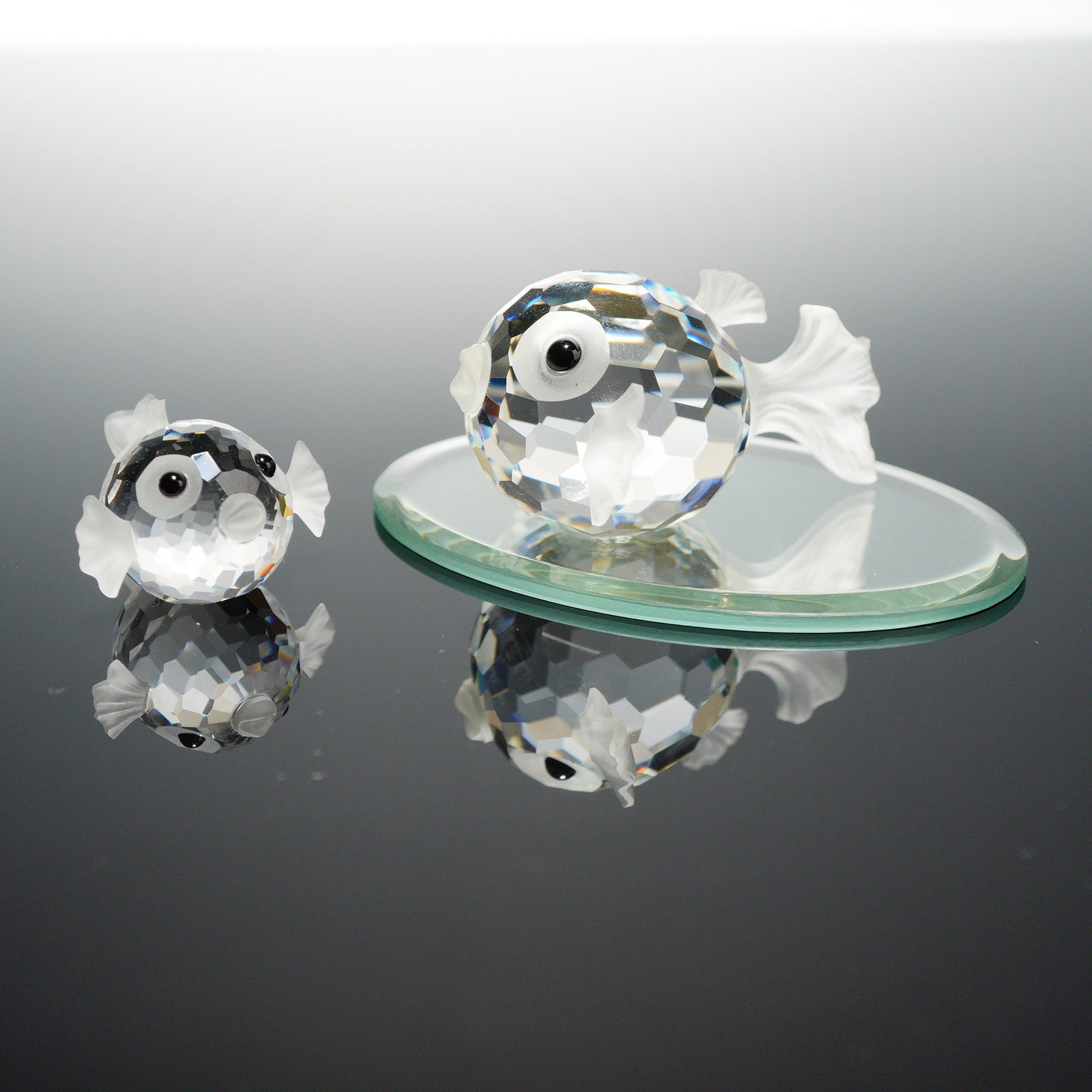 Lot of 2 Swarovski Silver Crystal Puffer Fish Figurines: This lot consists of two Swarovski Silver Crystal puffer fish figurines, also known as blowfish, in varying sizes. Both figurines feature a spherical, multi-faceted clear crystal body designed to refr