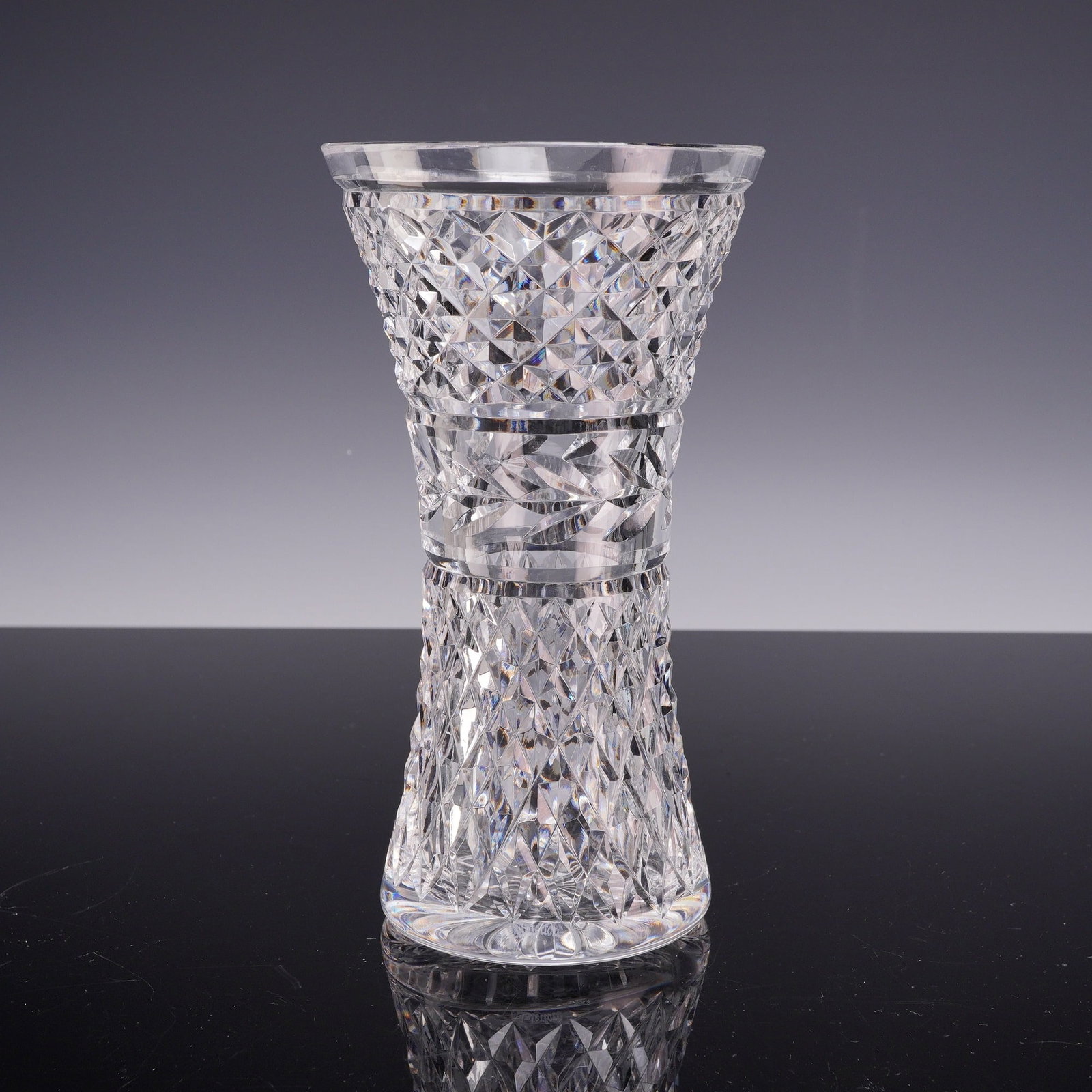 Waterford Crystal Glandore Pattern Flower Vase: A lead crystal vase by Waterford produced in the Glandore pattern. The vessel features a flared rim above a tapering neck, a constricted central waist, and a flared base. The body is decorated with mu