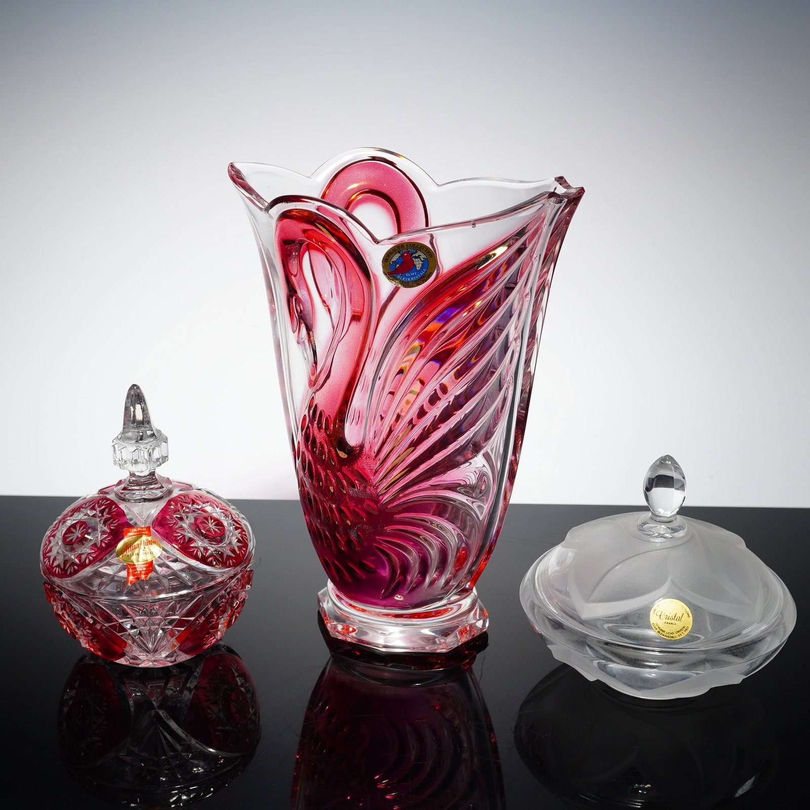 3pc French and German Lead Crystal Vase and Covered Bowls: This collection features a Hofbauer table vase crafted in clear and light-cranberry pink glass, depicting two swans in relief. Also included is a covered dish by Anna Hutte in clear and light-cranberr
