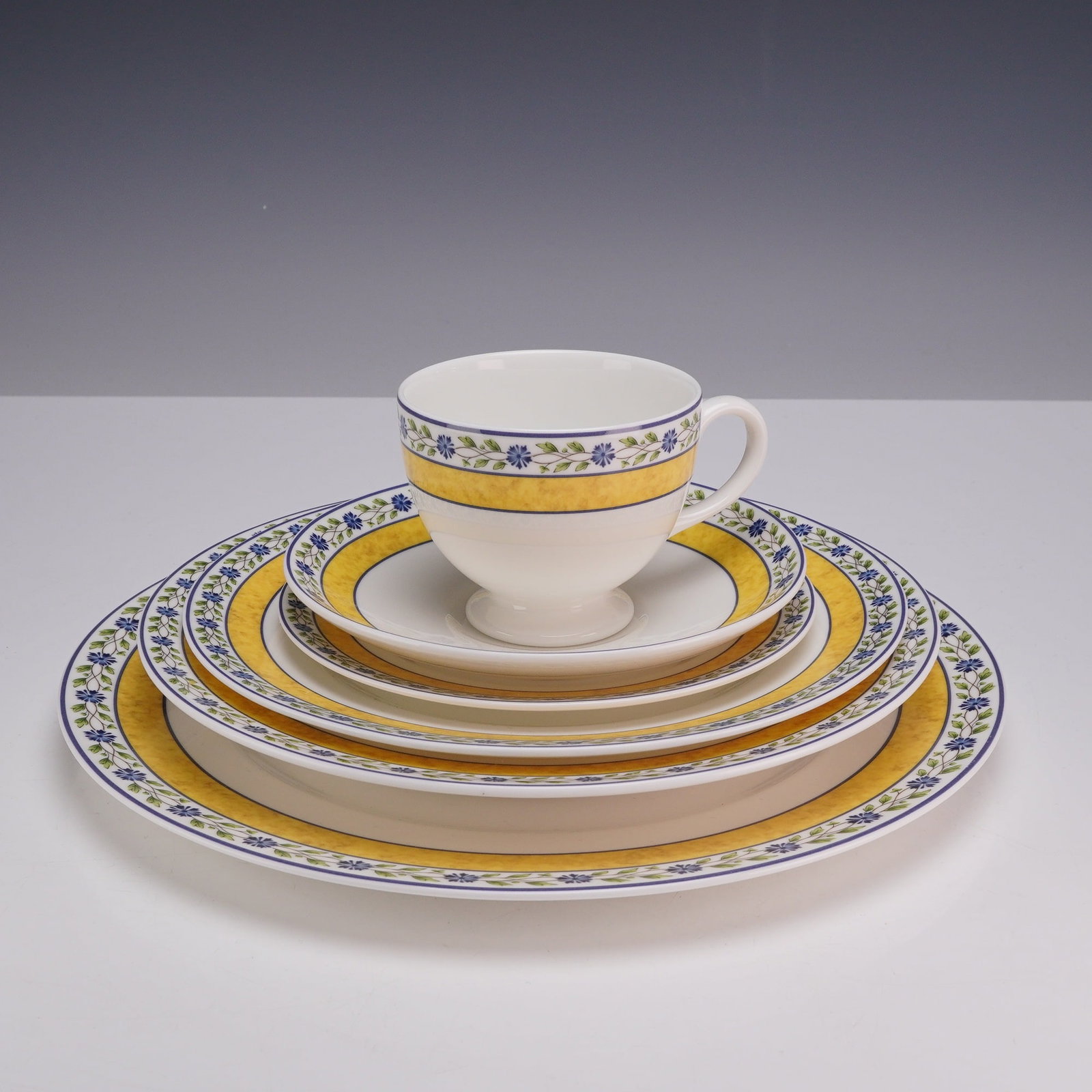 6 Piece Set of Wedgwood Bone China Plates and Teacup, Mistral: This is a 6 piece set of English bone china manufactured by Wedgwood in the Mistral pattern. The set features a contemporary design with a wide yellow marbled band, bordered by a floral vine motif of