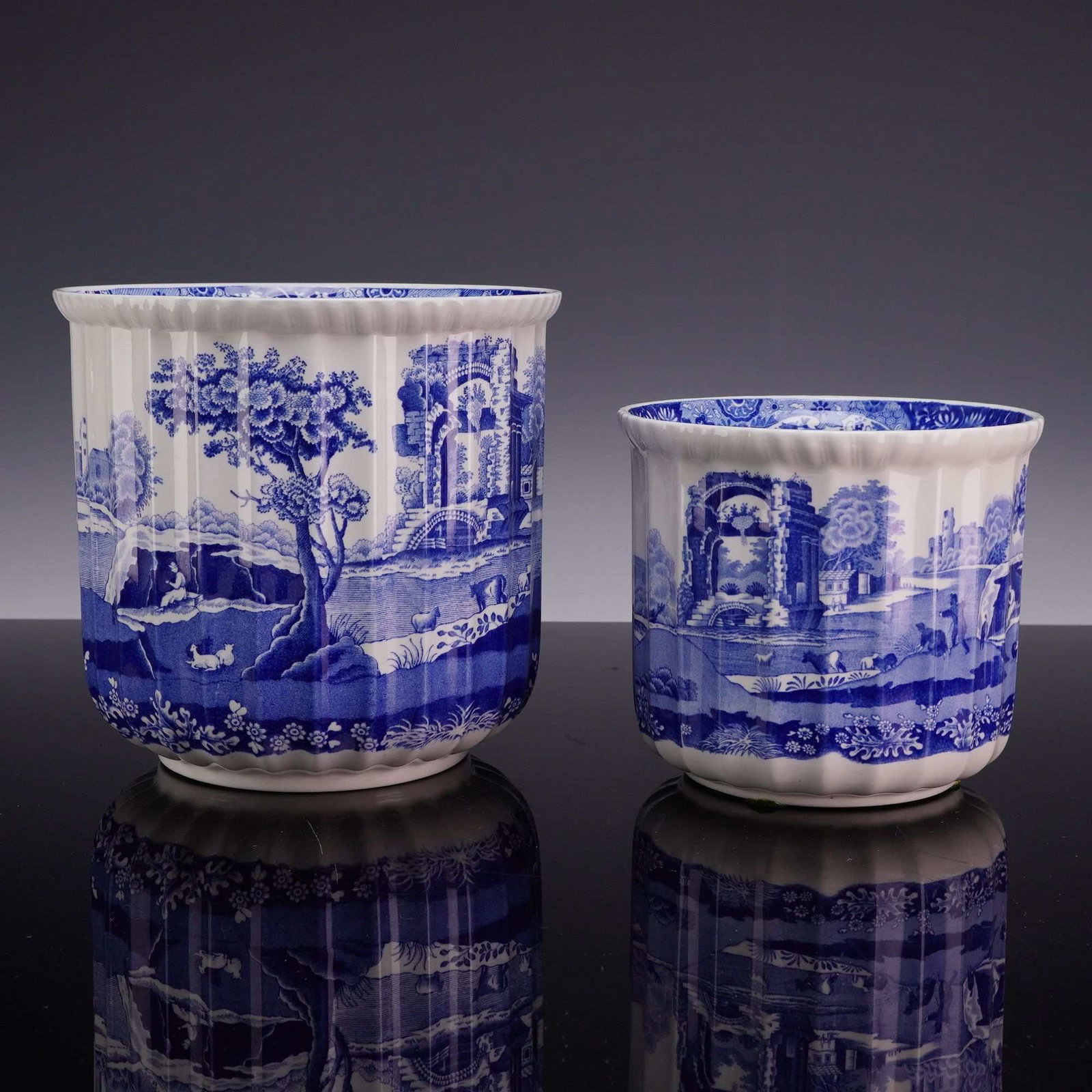 2pc Spode Blue Italian Graduated Earthenware Cachepots: A pair of graduated earthenware cachepots by Spode in the Blue Italian pattern. Each vessel features a cylindrical body with vertical fluting, a scalloped rim, and a slightly tapered base. The exterio