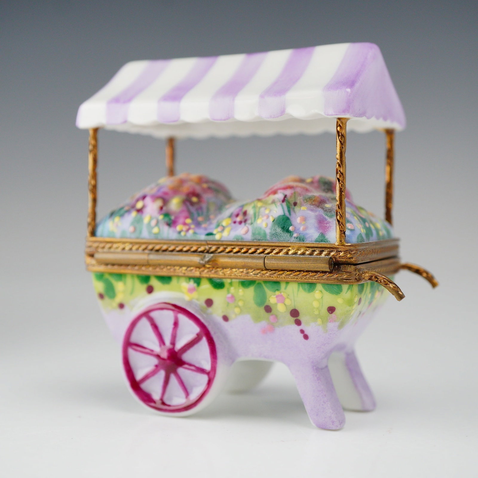 Parry Vieille Hand Painted Porcelain Flower Cart Limoges Treasure Box: This porcelain Limoges treasure box is crafted as a miniature flower cart by the Parry Vieille. The piece features a hinged lid and a gold-tone metal frame secured with a flowers in a vase clasp. The 
