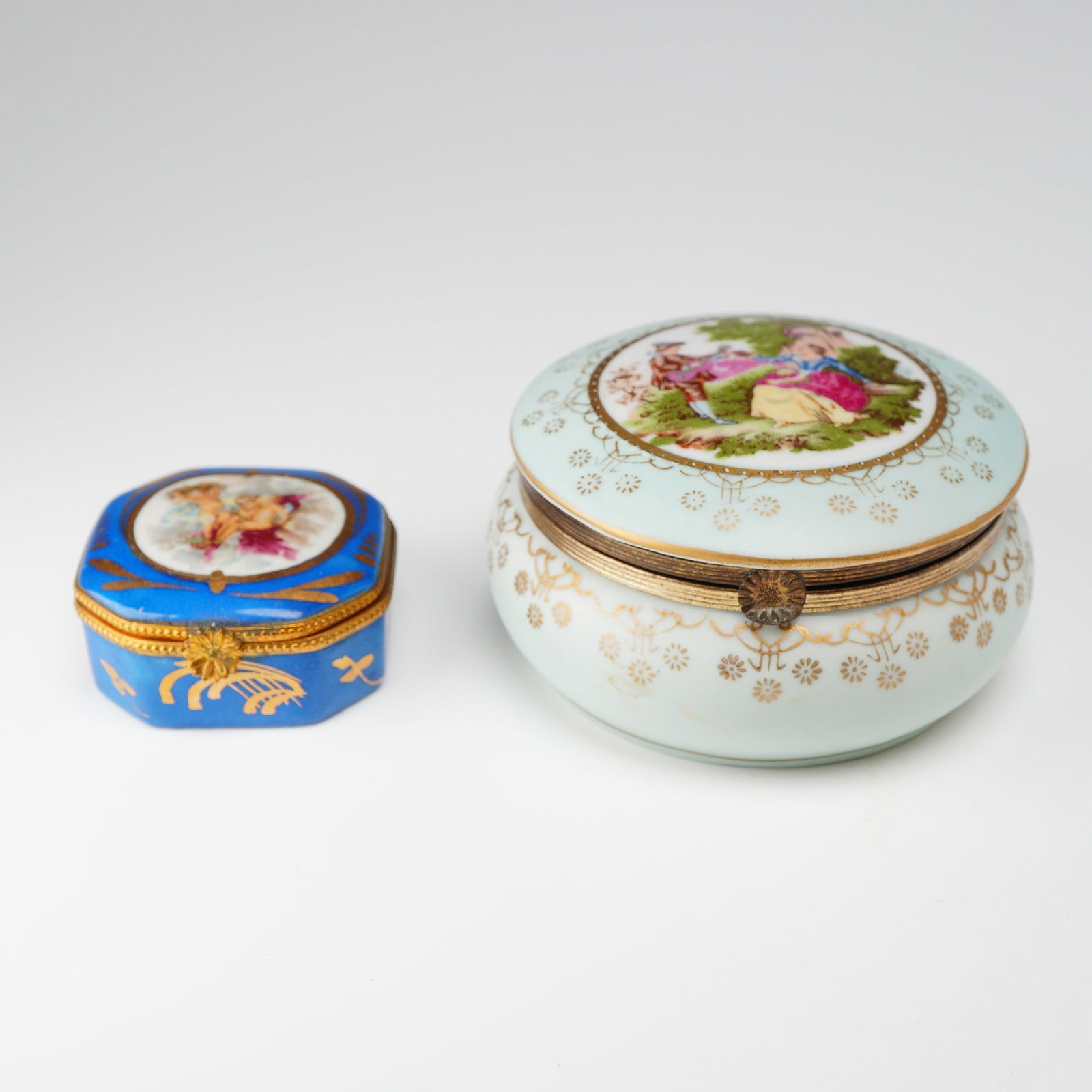 Lot of Two Vintage Porcelain Trinket Boxes Including Limoges France: This lot features two vintage porcelain hinged trinket boxes of European design. The first is a small octagonal-lobed box featuring a vibrant cobalt blue ground. It is decorated with gilded foliate an
