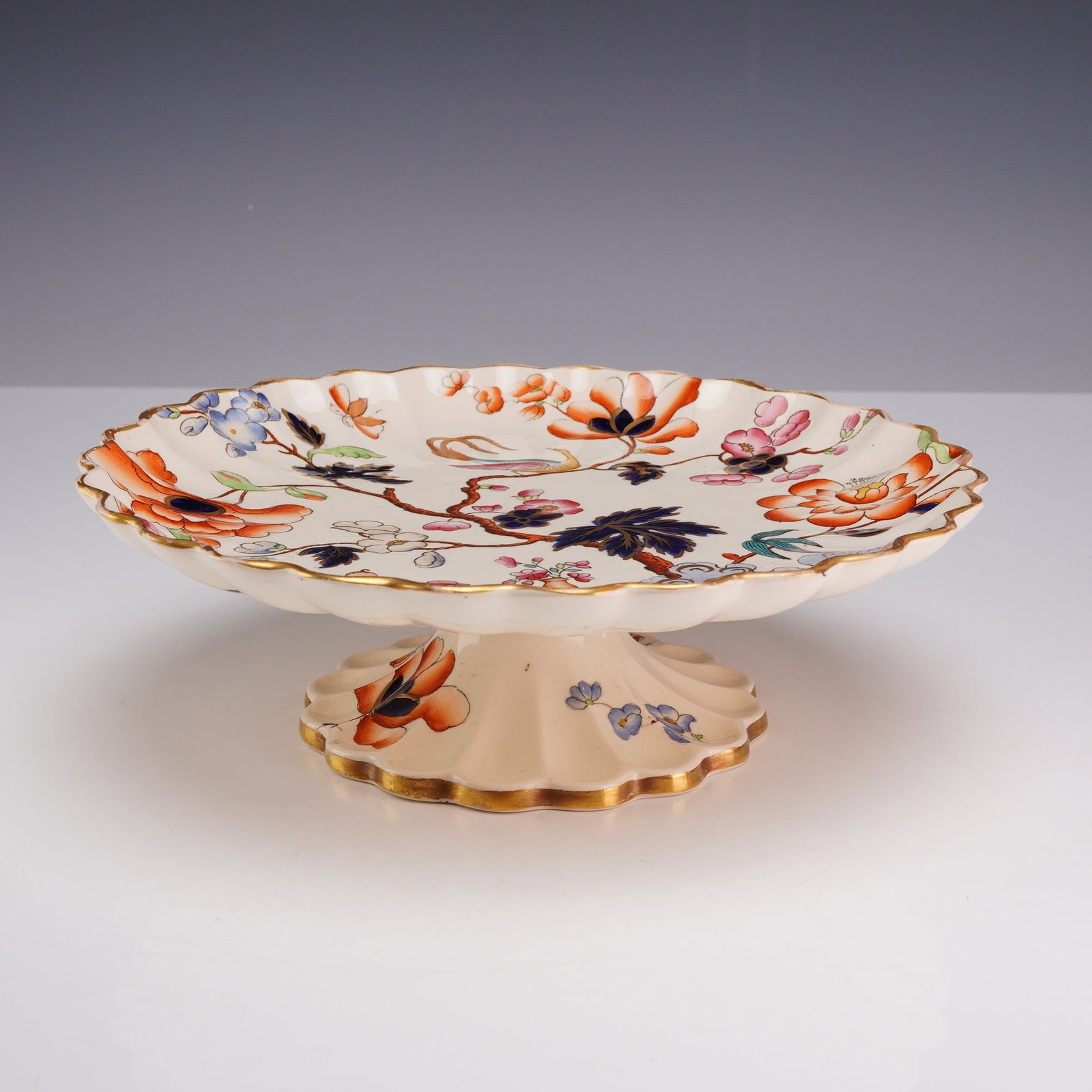 Copeland Small Footed Ceramic Cake Stand: A W.T. Copeland and Sons ceramic small cakestand featuring a circular plate with a deeply scalloped and lobed rim, mounted on a matching pedestal foot. The interior surface is decorated with a vibrant