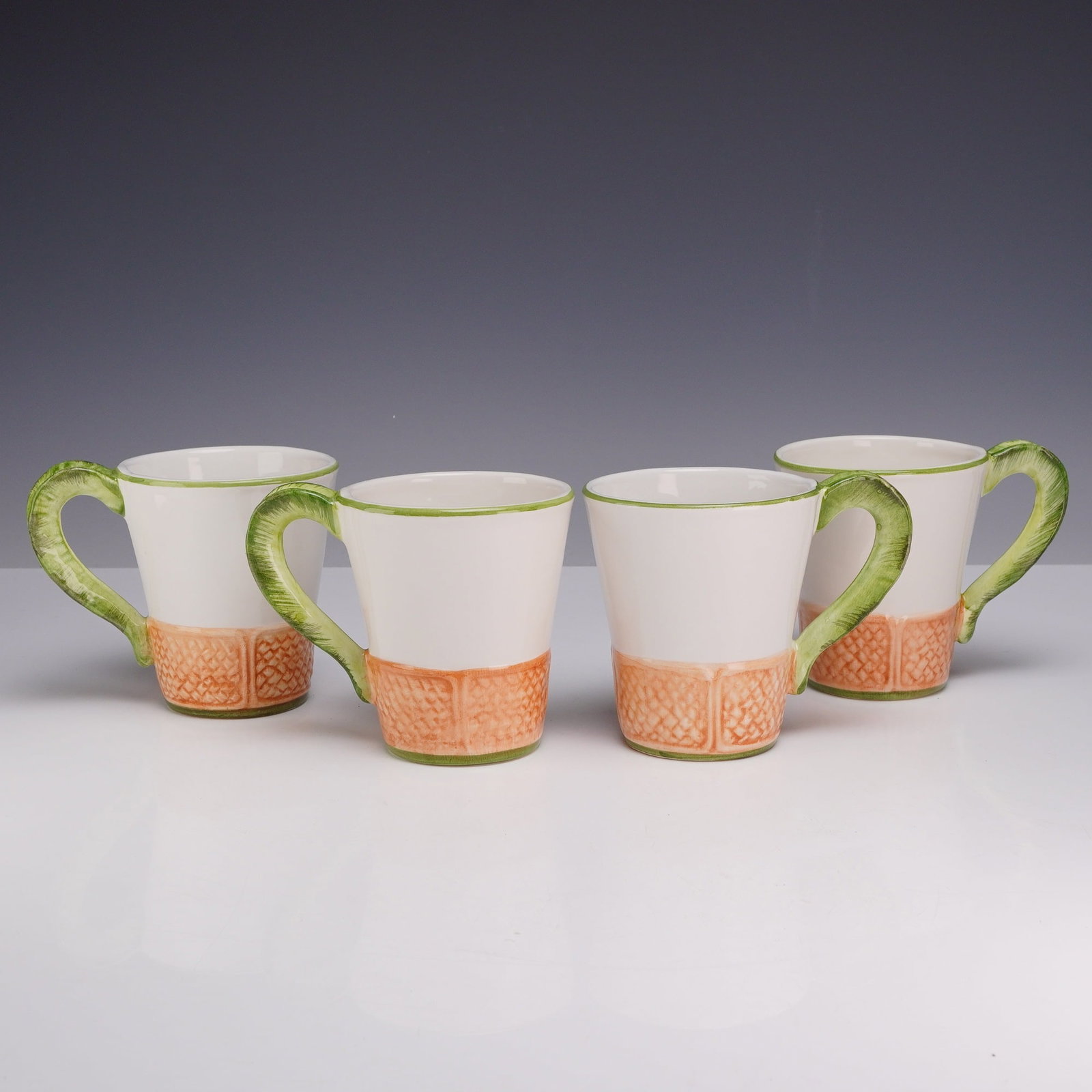 4pc Vietri Italian Mugs, Oasi: A set of four handcrafted Italian ceramic mugs produced for Vietri. Each mug features a tapered, flared body with a white glazed upper portion. The lower section is decorated with a molded relief patt