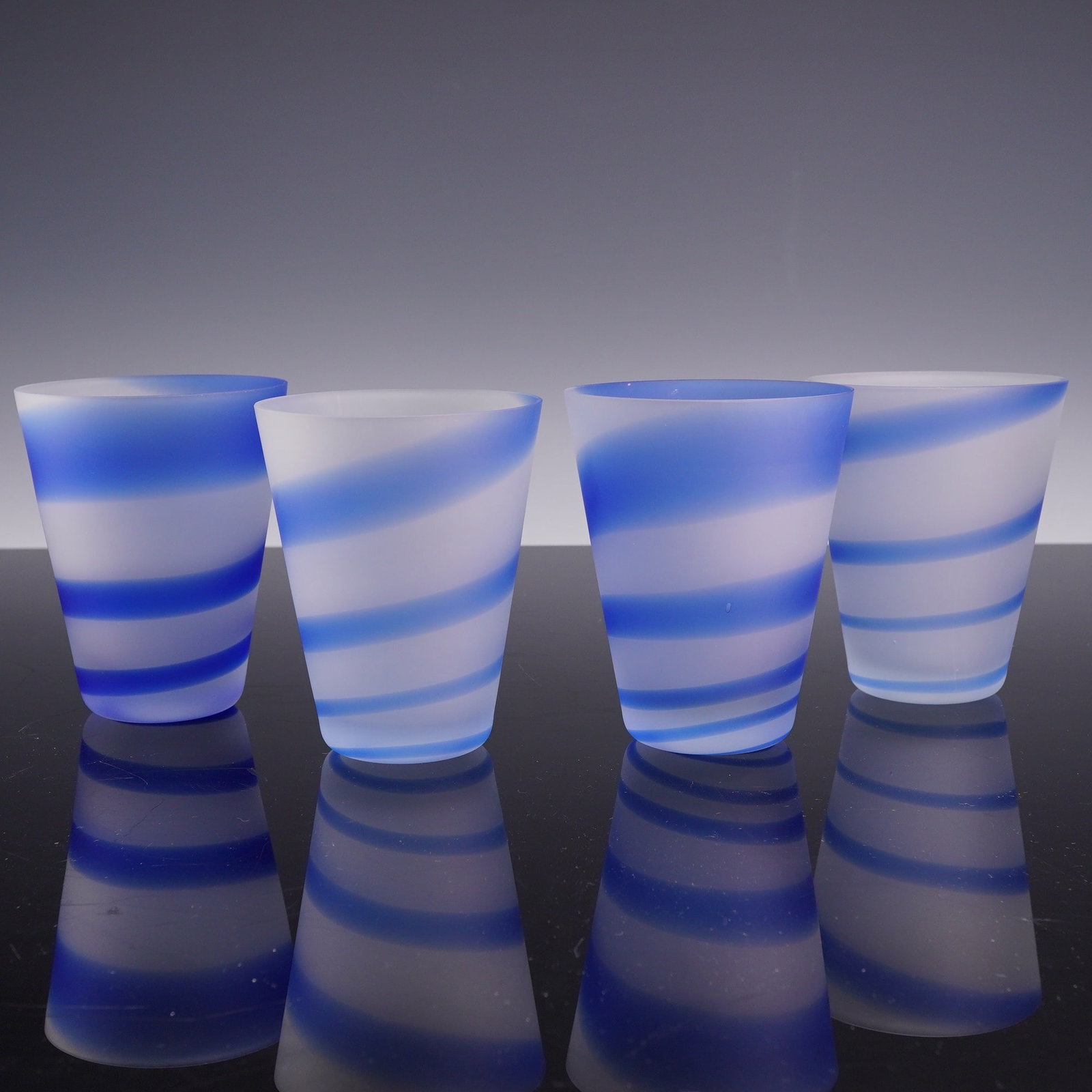 4pc Frosted Glass Tumblers with Blue Spiral Decoration: This set of four glass tumblers features a tapered cylindrical form with a frosted or satin finish. Each tumbler is decorated with a vibrant blue stripe that spirals around the body from the rim to