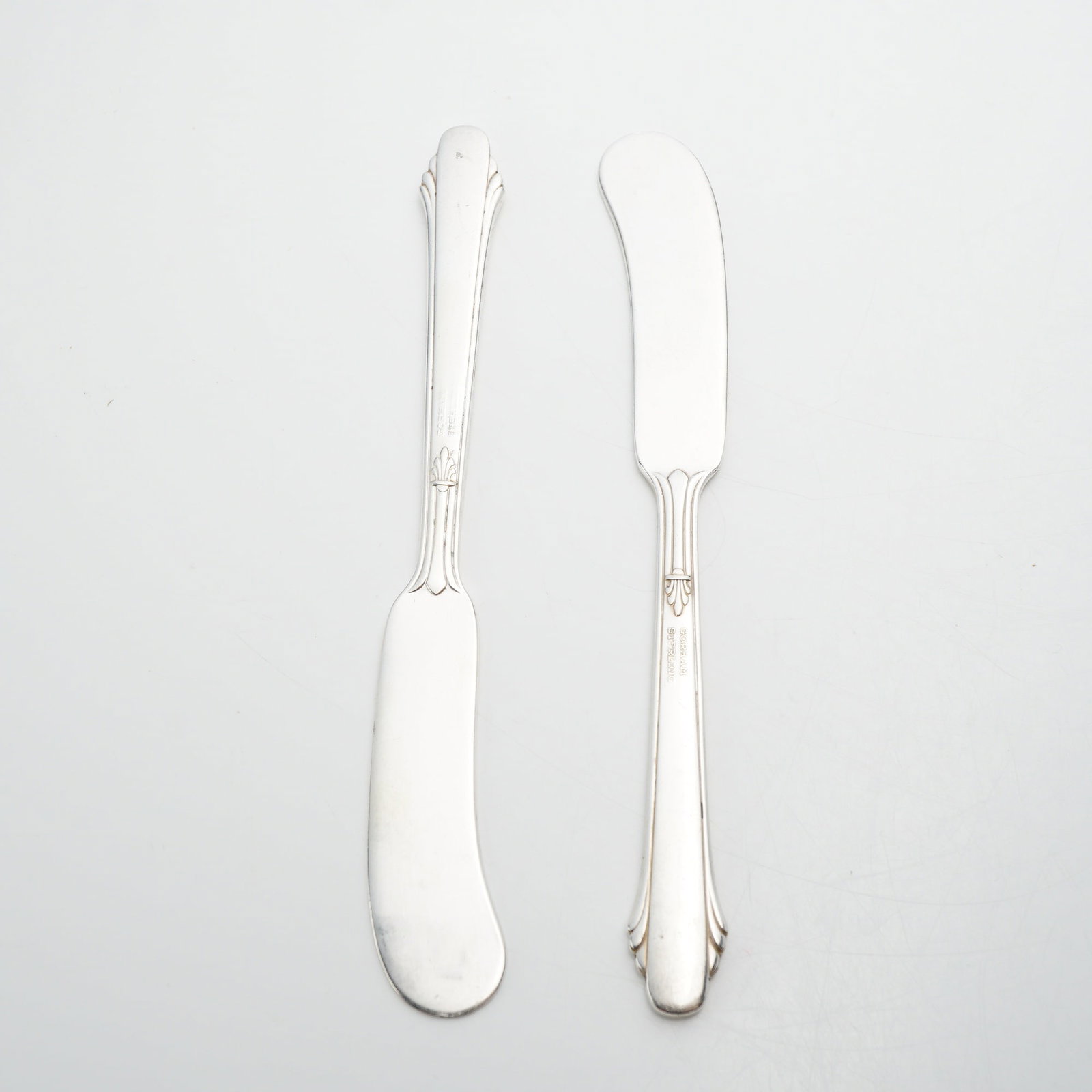 Pair of Gorham Sterling Silver Flat Handle Butter Spreader Knives: The spreaders are constructed from solid sterling silver. The design features a linear handle with parallel border lines terminating in a stylized shell motif at the bolster. The front of each handle 