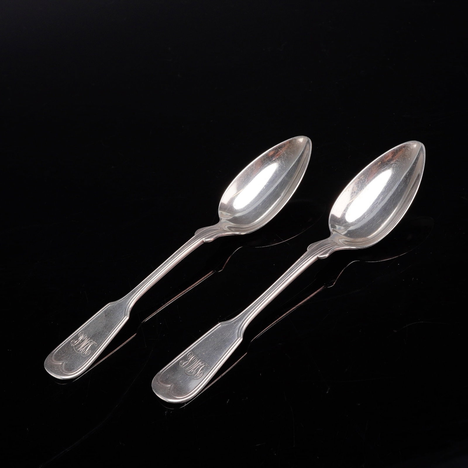 A Pair of W. Carrington & Co. Sterling Silver Fiddle Thread Pattern Spoons: A pair of sterling silver spoons rendered in the fiddle thread pattern, which includes a double-threaded border along the handle edges and shoulders. Each handle terminal features an ornate script mon