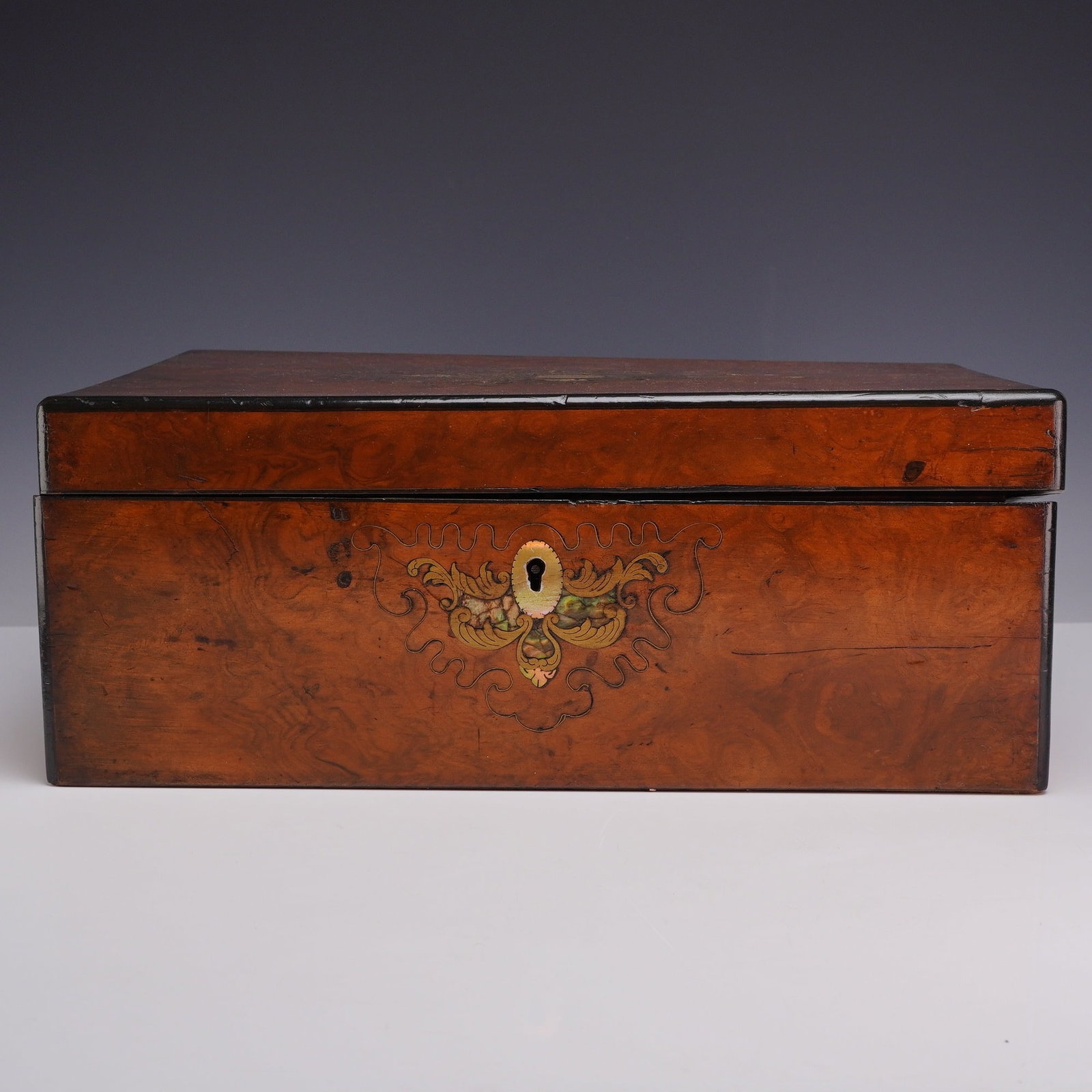 Victorian Wooden Traveling Writing Desk with Ornate Inlay of Brass and Mother-of-Pearl: This 19th-century Victorian wooden traveling writing desk features a rich burl veneer accented by ebonized borders. The front of the box is decorated with an ornate foliate inlay of brass and mother-o