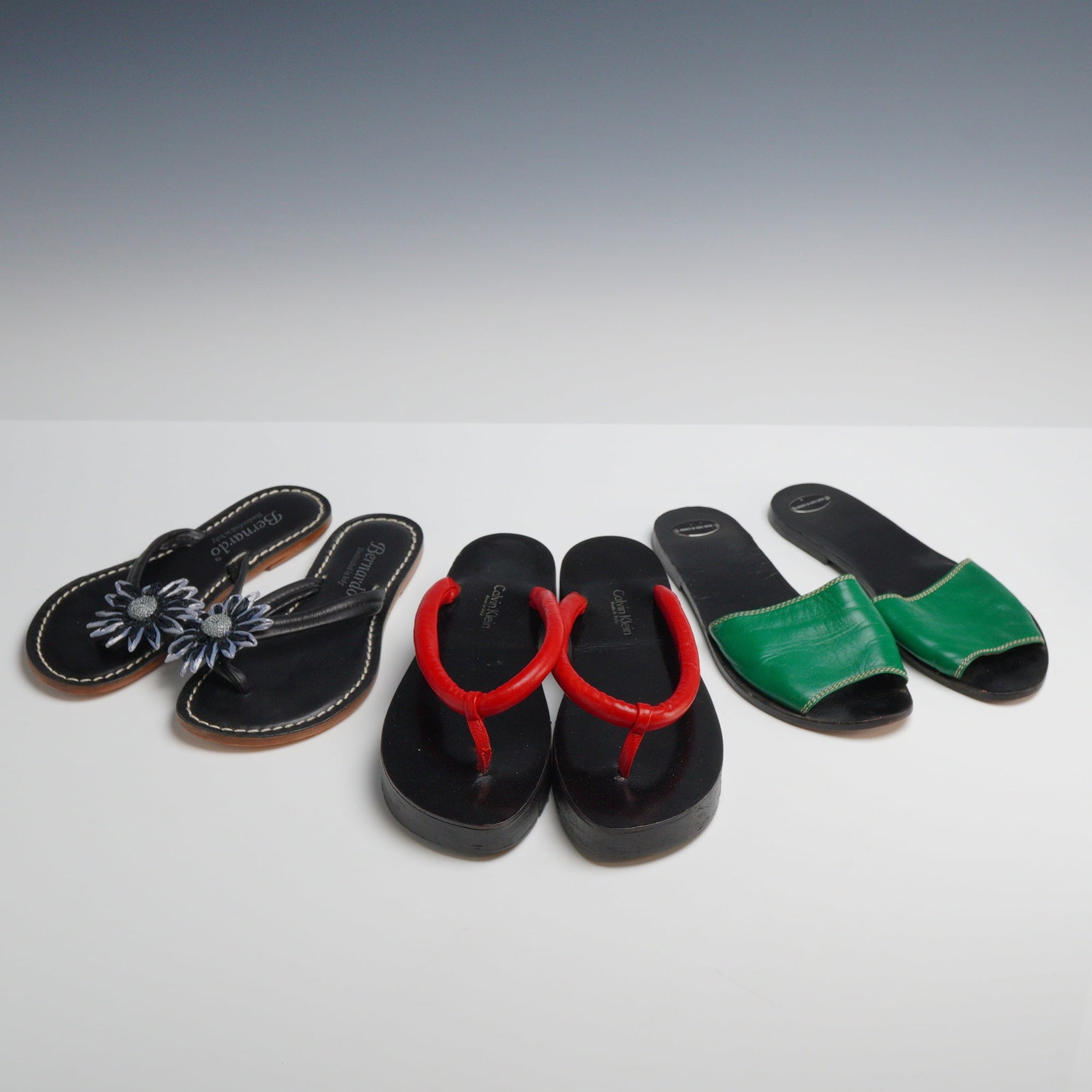 Three Pairs of Designer Summer Sandals: Calvin Klein, Bernardo, and Fausto Santini: This lot features three pairs of Italian-made designer summer slides and shoes. The first pair consists of Bernardo Miami thong sandals, size 5M, handcrafted in Italy from black leather with white con