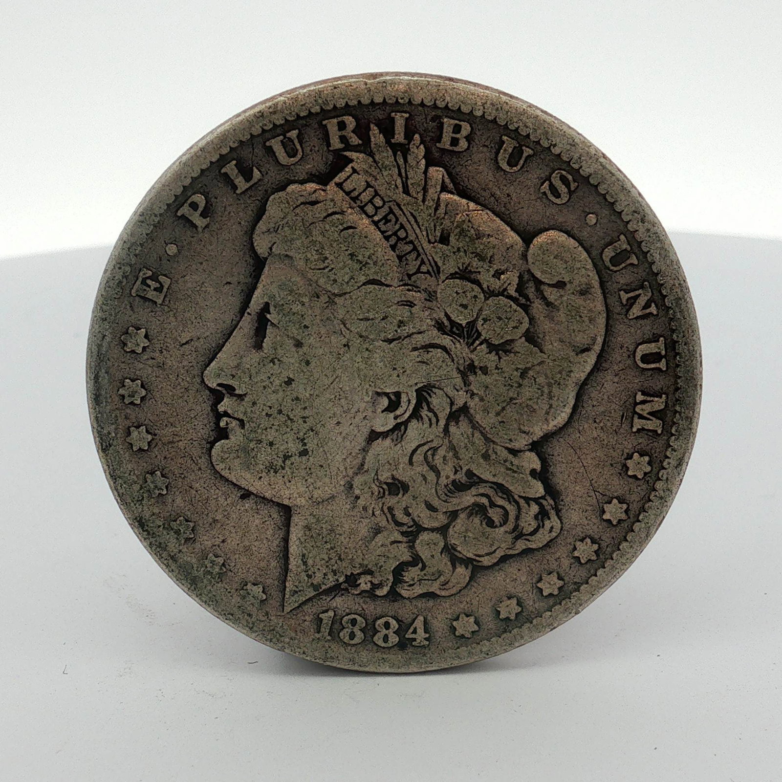 1884 US One Dollar Morgan Silver Dollar, Circulated: This 1884 US Morgan silver dollar was struck at the Philadelphia Mint. The coin is composed of 90 percent silver and 10 percent copper. The obverse features the Liberty Head design with the date 1884 