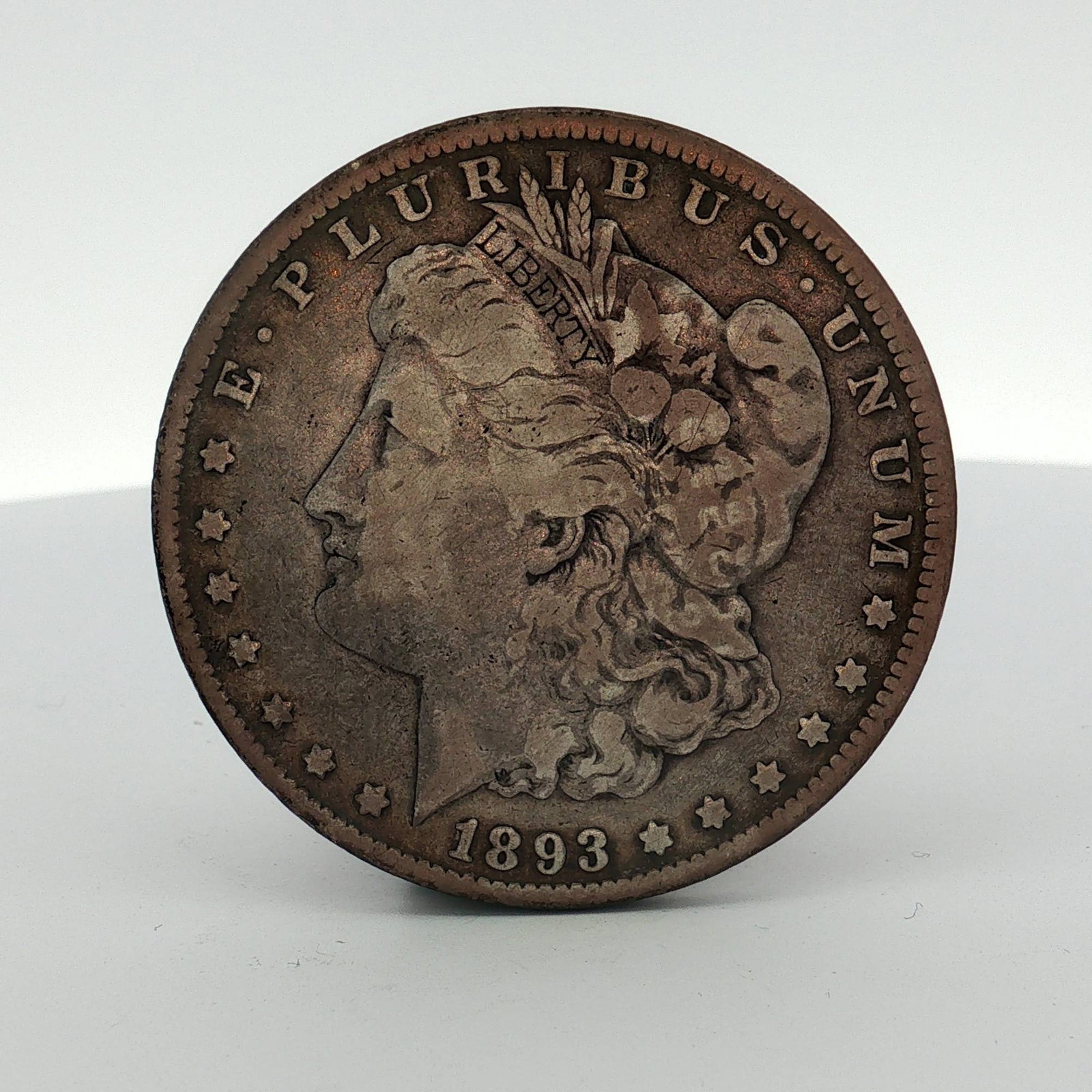 1893 US Morgan Silver Dollar: 1893 US Morgan silver dollar struck in 90 percent silver. The obverse bears the Morgan dollar design with the date 1893 and the legend E PLURIBUS UNUM. The reverse features the heraldic eagle design w