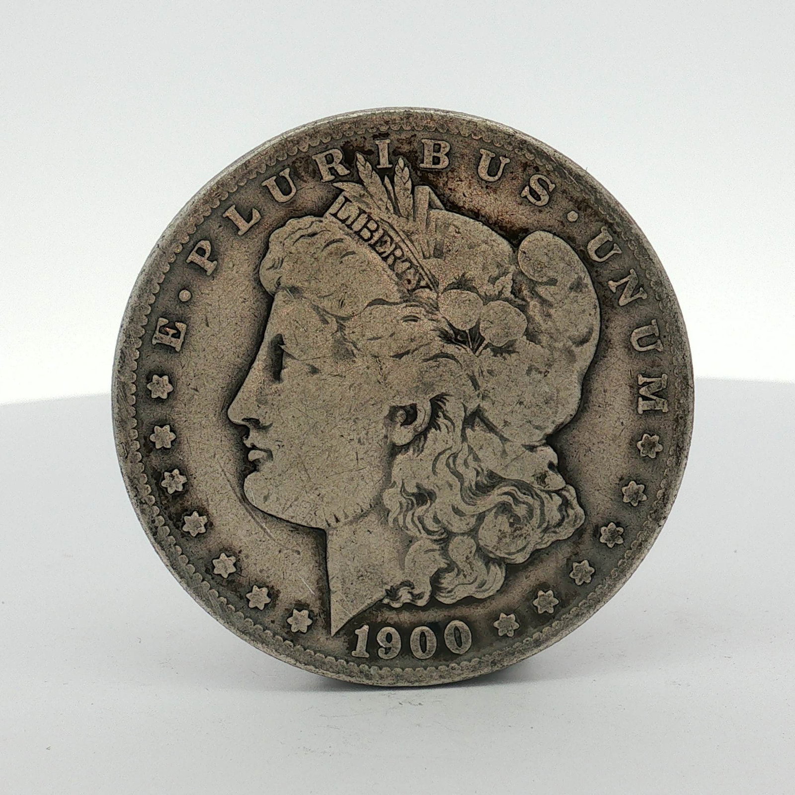 1900-S US One Dollar Morgan Silver Dollar, Circulated: This US 1900-S Morgan silver dollar was struck at the San Francisco Mint. The coin is composed of 90% silver and 10% copper. It features the Morgan dollar design with the S mint mark located on the re