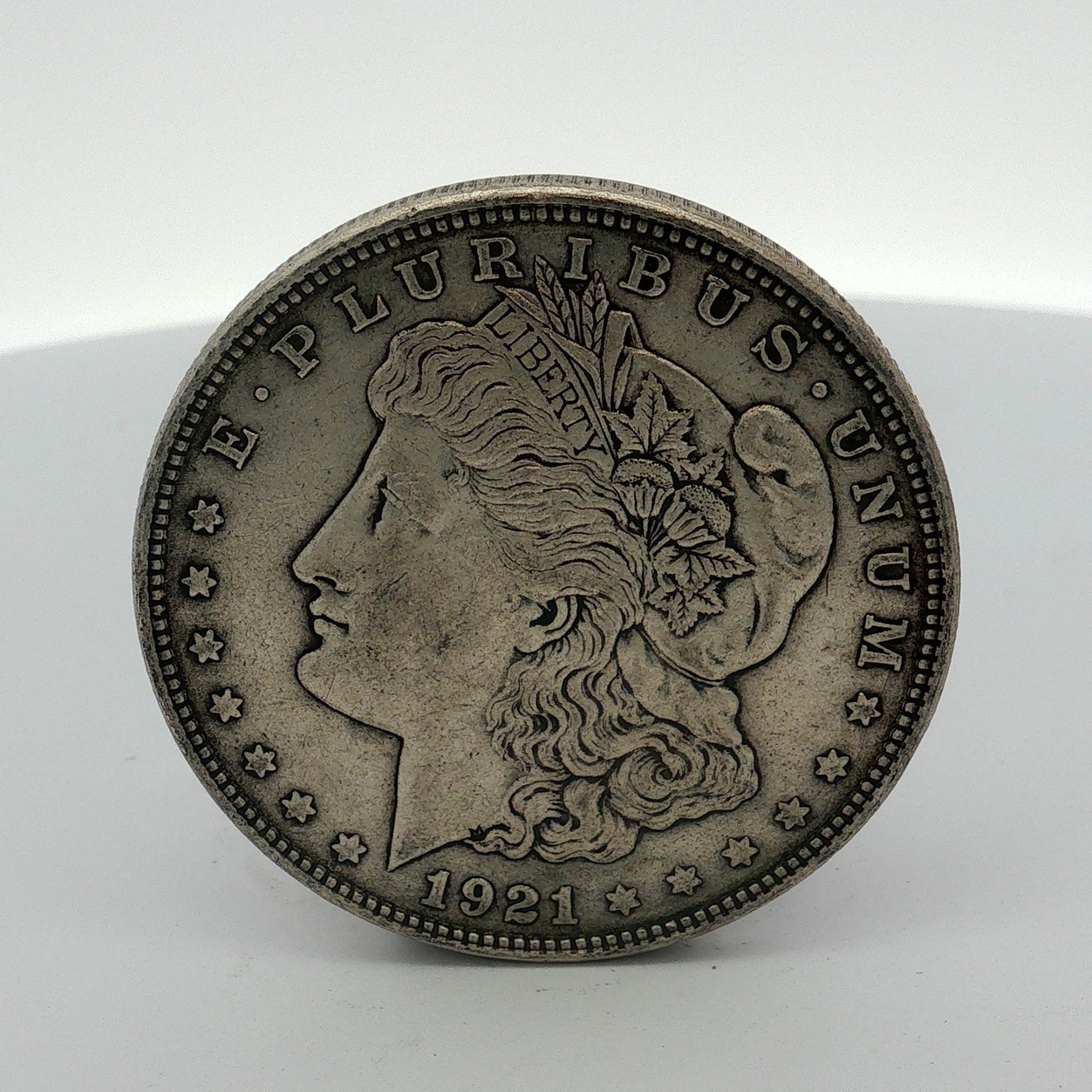 1921 US Morgan Silver Dollar Coin Circulated: This 1921 US silver Morgan dollar is a Philadelphia mint issue, as indicated by the absence of a mint mark on the reverse. The coin features the Morgan dollar design type and is composed of 90 percent