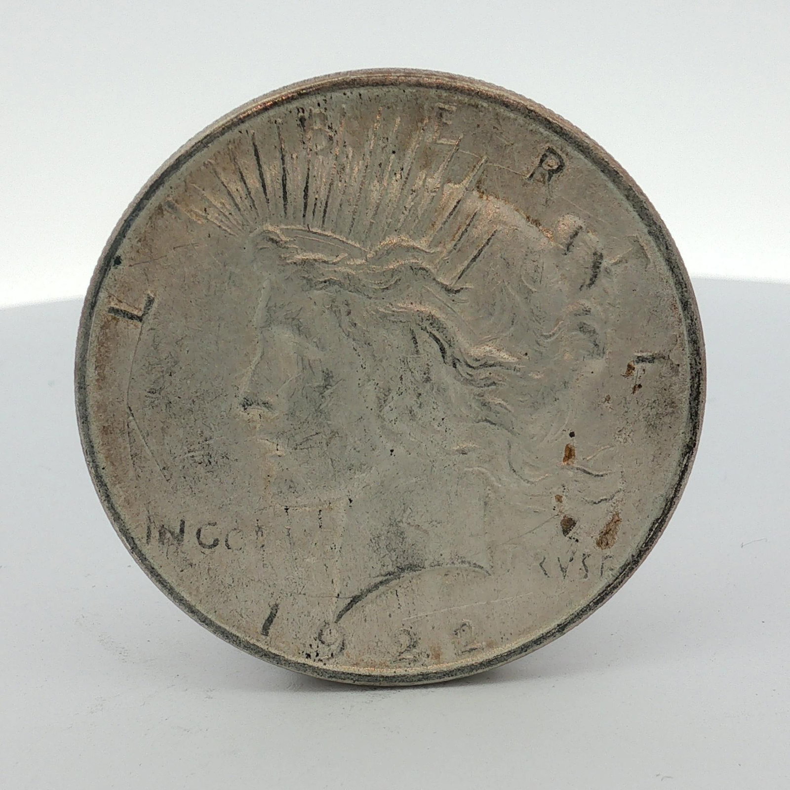 1922-D US One Dollar Peace Silver Dollar, Circulated: 1922 US Peace silver dollar. This coin is composed of 90% silver and 10% copper. It was struck at the Denver Mint, as evidenced by the D mint mark above tail feathers. The coin features the Peace doll