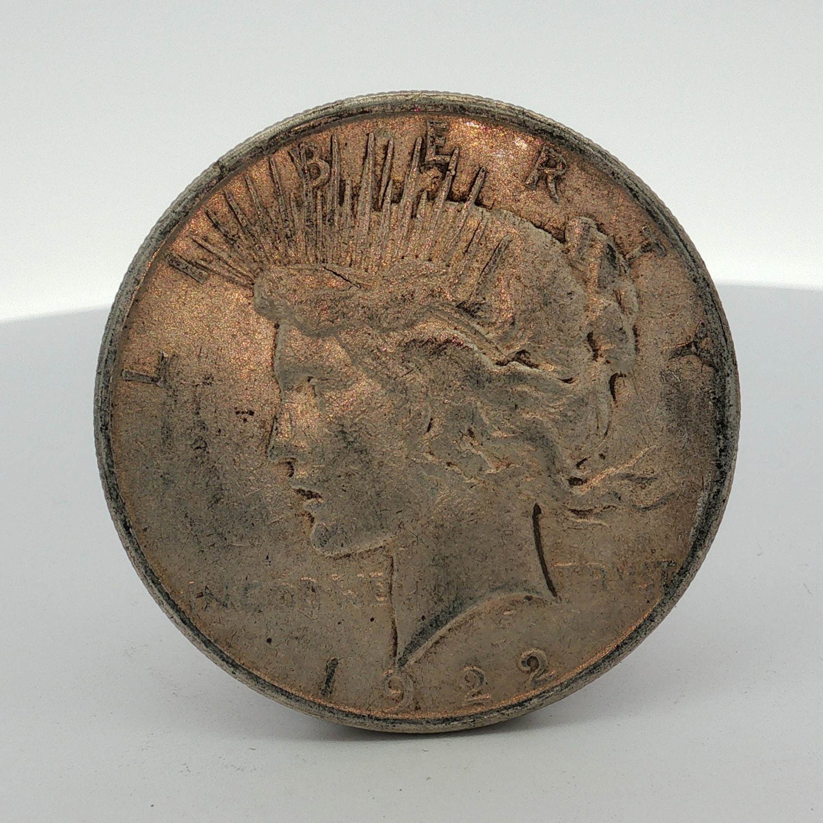 1922-S US One Dollar Peace Silver Dollar Coin, Circulated: A 1922 United States Peace silver dollar composed of 90% silver and 10% copper with a reeded edge. The coin features the Peace type obverse and reverse designs by Anthony de Francisci. Obverse inscrip