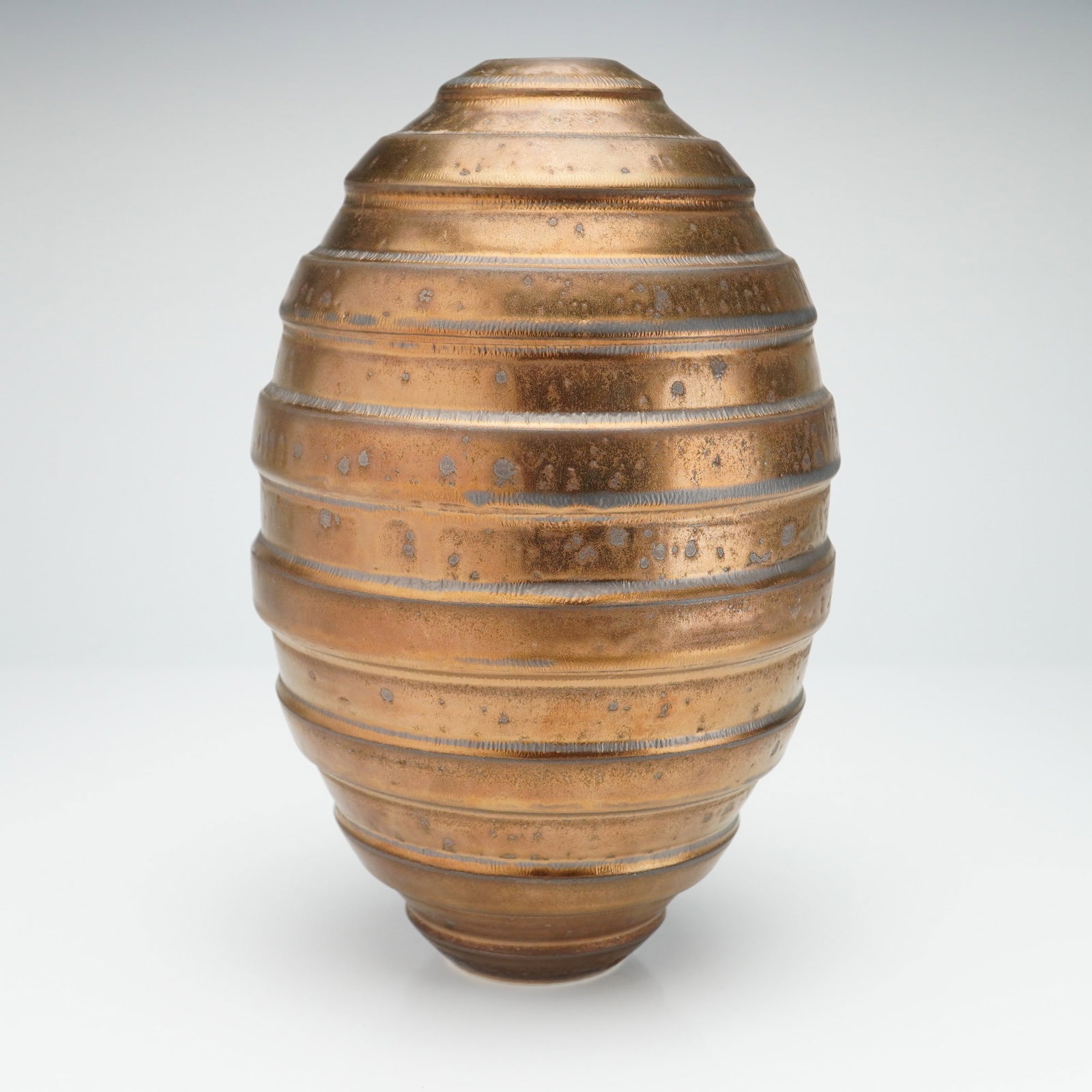 John Parker Gold Luster Glazed Grooved Vase: This spiral, grooved vase is of ovoid form, characterized by a series of horizontal concentric ridges that create a stepped or beehive profile. The vessel tapers from its widest point at the mid-secti