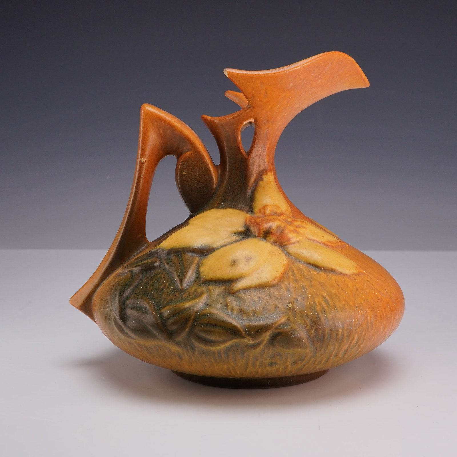 Roseville Pottery Clematis Pattern Ewer 16-6: An American art pottery ewer in the Clematis pattern, manufactured by the Roseville Pottery Company of Zanesville, Ohio. Introduced in 1944, this piece features a low, bulbous body with a textured, ba
