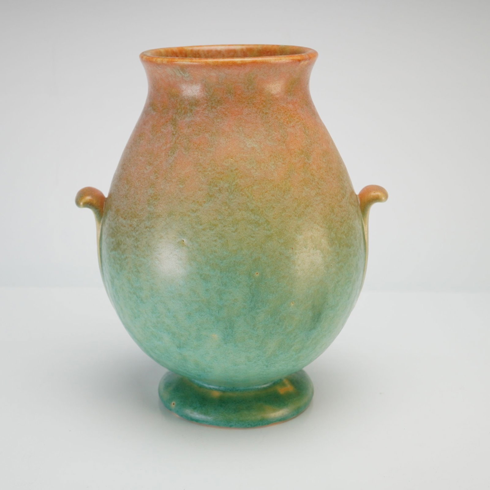 Weller Pottery Art Deco Mottled Glaze Ceramic Vase: This Weller Pottery earthenware vase features an ovoid body with a flared rim, supported by a short pedestal foot. Two small scroll handles are attached at the shoulders. The exterior is finished in a