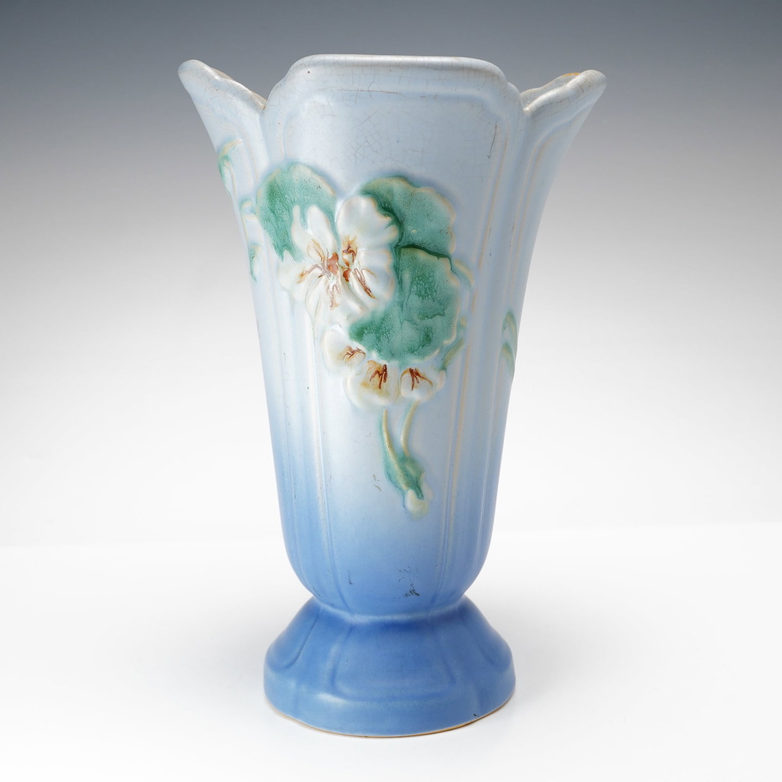 Weller Pottery Wild Rose Pattern Blue Ombre Flared Vase: This American art pottery vessel is produced by Weller Pottery. The earthenware vase is decorated in the Wild Rose pattern, featuring a molded relief of a white blossom with a yellow center and green 