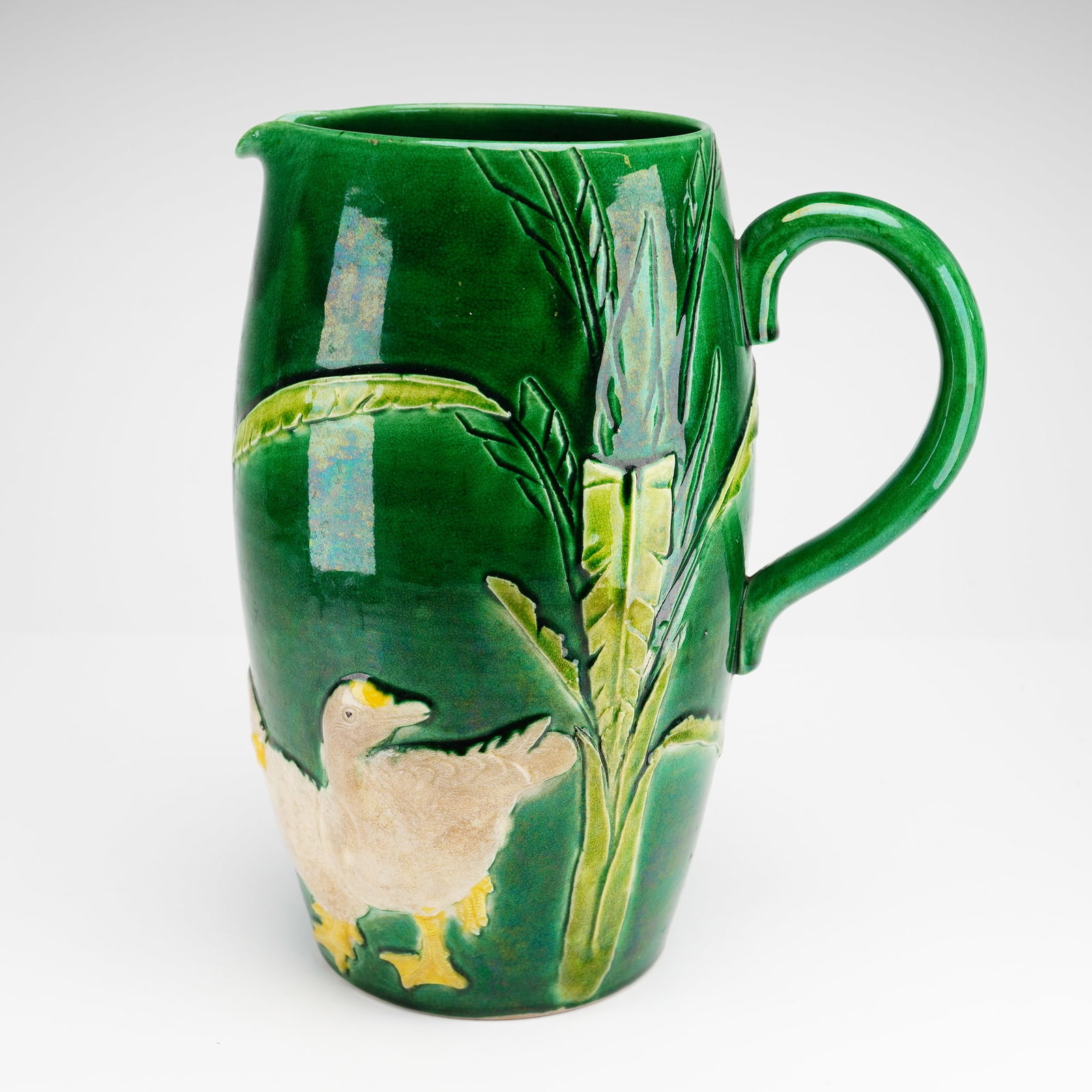 Majolica Earthenware Pitcher with Ducks: A tapering earthenware pitcher featuring relief-molded decoration in the majolica style. The body is finished in a vibrant, high-gloss emerald green glaze. The primary decorative motif consists of two