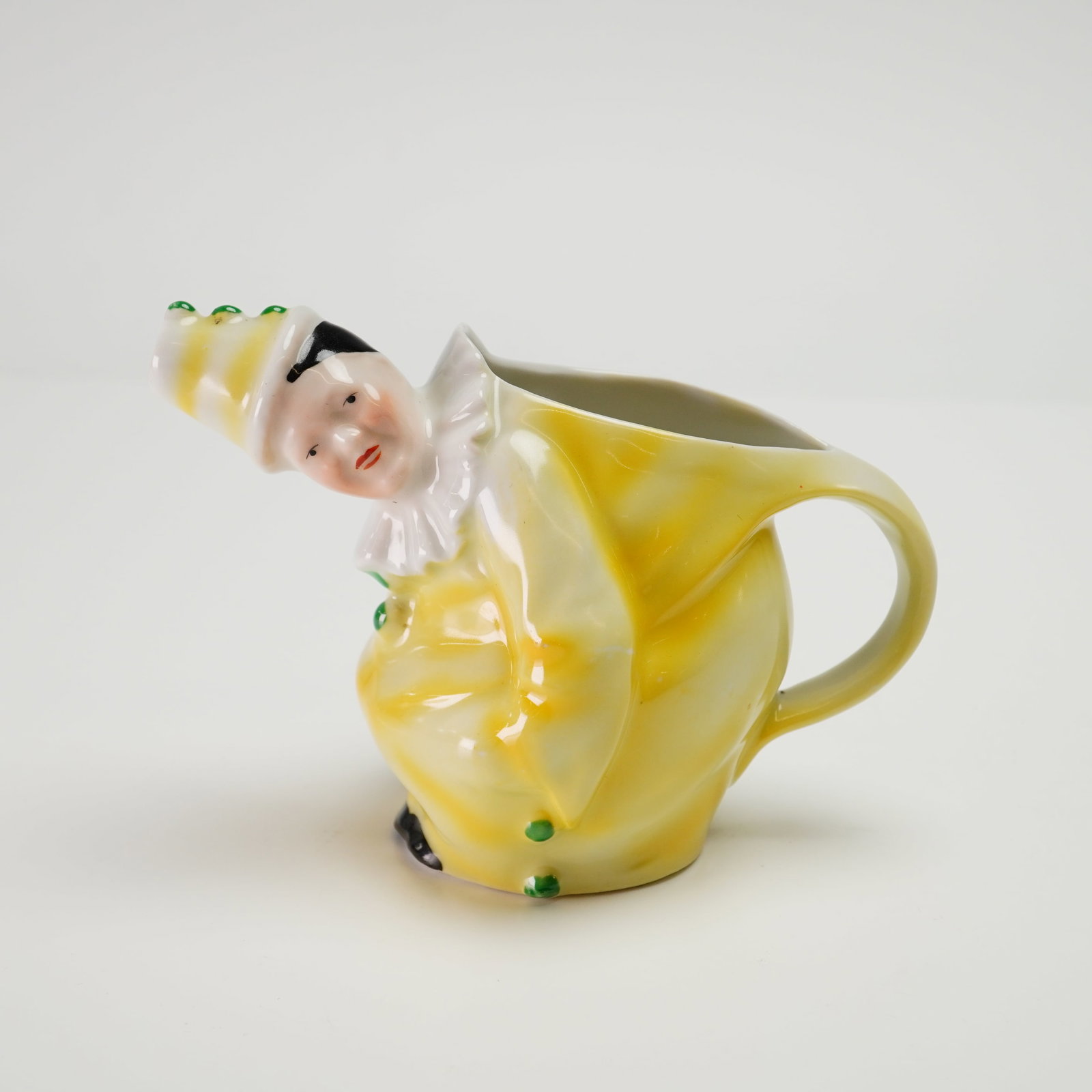 Royal Bayreuth Small Yellow Clown Porcelain Creamer: A figural porcelain creamer designed in the form of a crouching clown. This piece features a vibrant yellow glaze over a molded porcelain form. The figure is depicted with hand-painted facial features