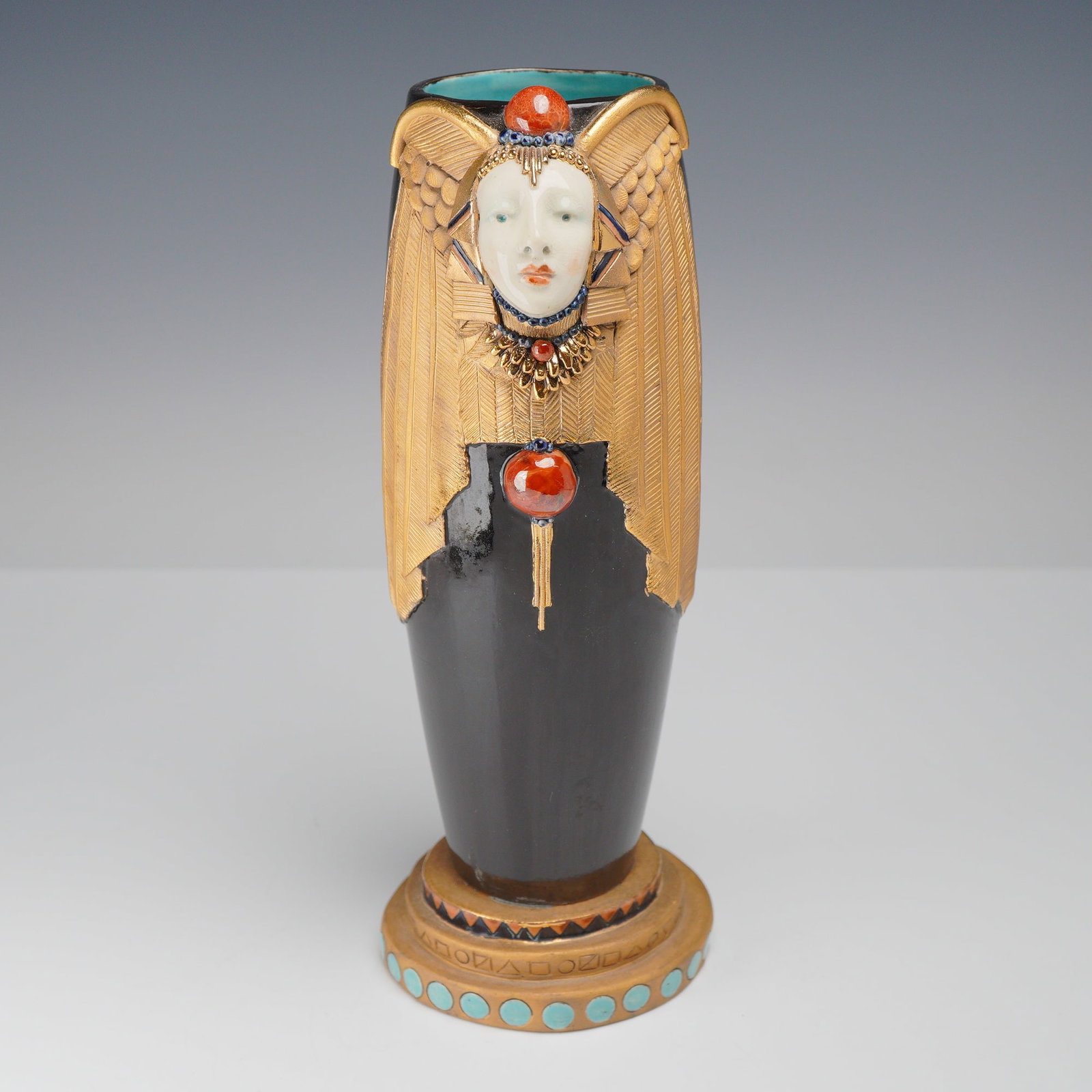 Postmodern Egyptian Revival Studio Ceramic Vase by Roberta, 1982: A tall, cylindrical studio pottery vase featuring a high-gloss black glazed exterior and a contrasting turquoise-blue glazed interior. The front of the vessel is decorated with a central relief-molded