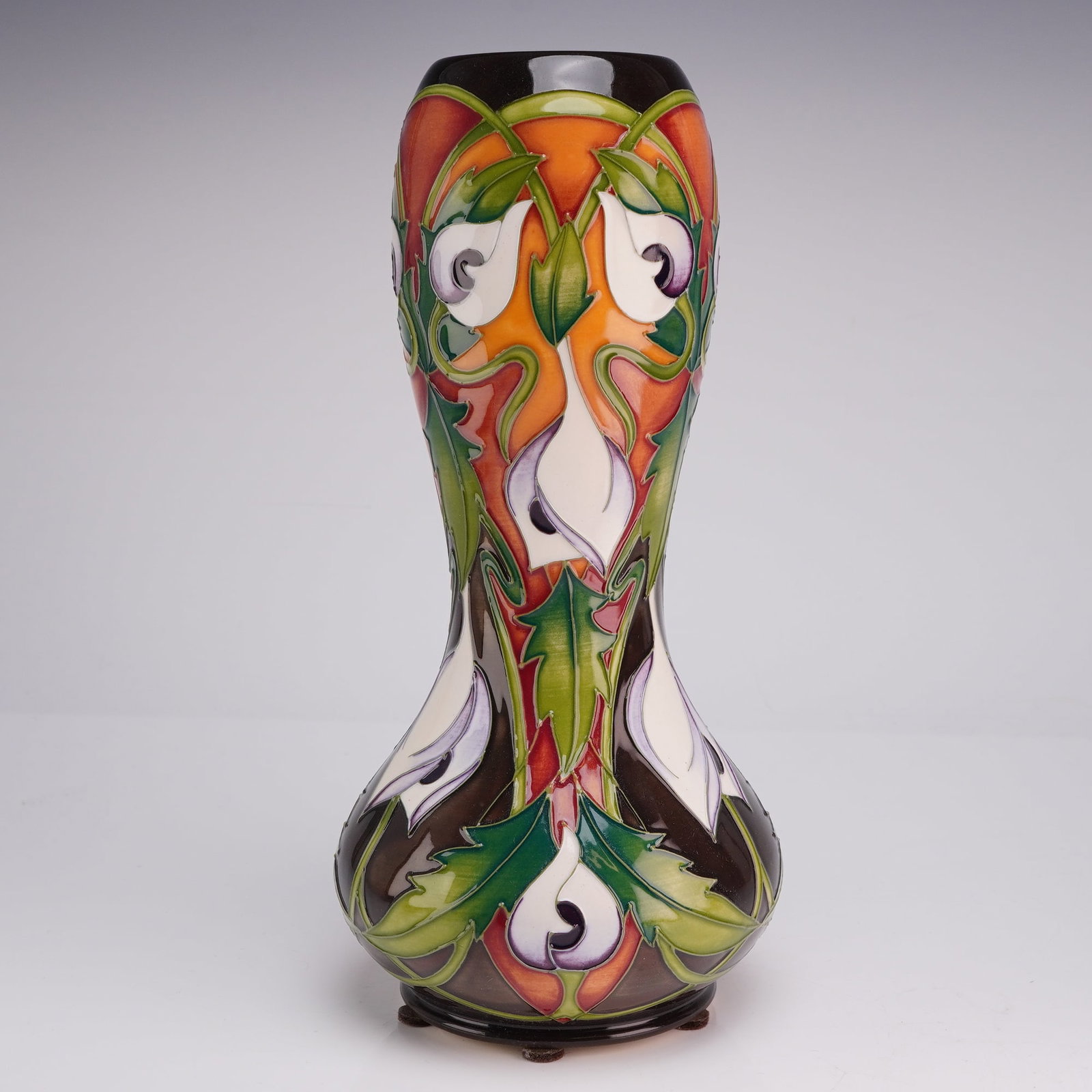 Moorcroft Tube-Lined Ceramic Vase Signed by Joanne B. Mountford Dated 2006: A contemporary earthenware vase of waisted baluster form produced by Moorcroft. The exterior features a hand-painted and tube-lined floral motif of stylized calla lilies with sharp, jagged foliage in 