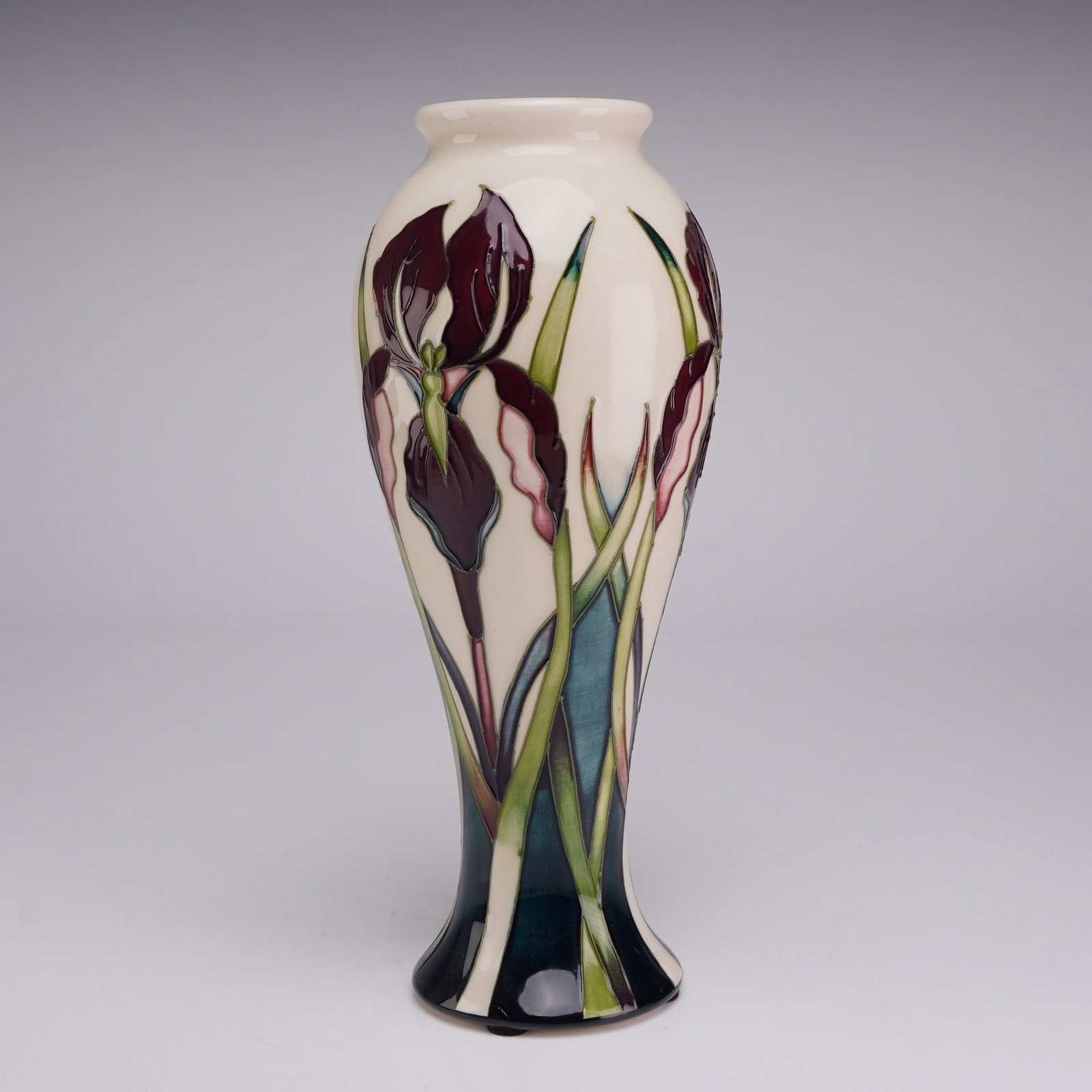 Moorcroft Pottery by Nicola Slaney Collectors Club 2009 Vase, Purple Iris: This slender, elongated earthenware vessel is characterized by a waisted neck, rolled rim, and flared base. The exterior is decorated using the tube-lining technique, featuring stylized irises in deep