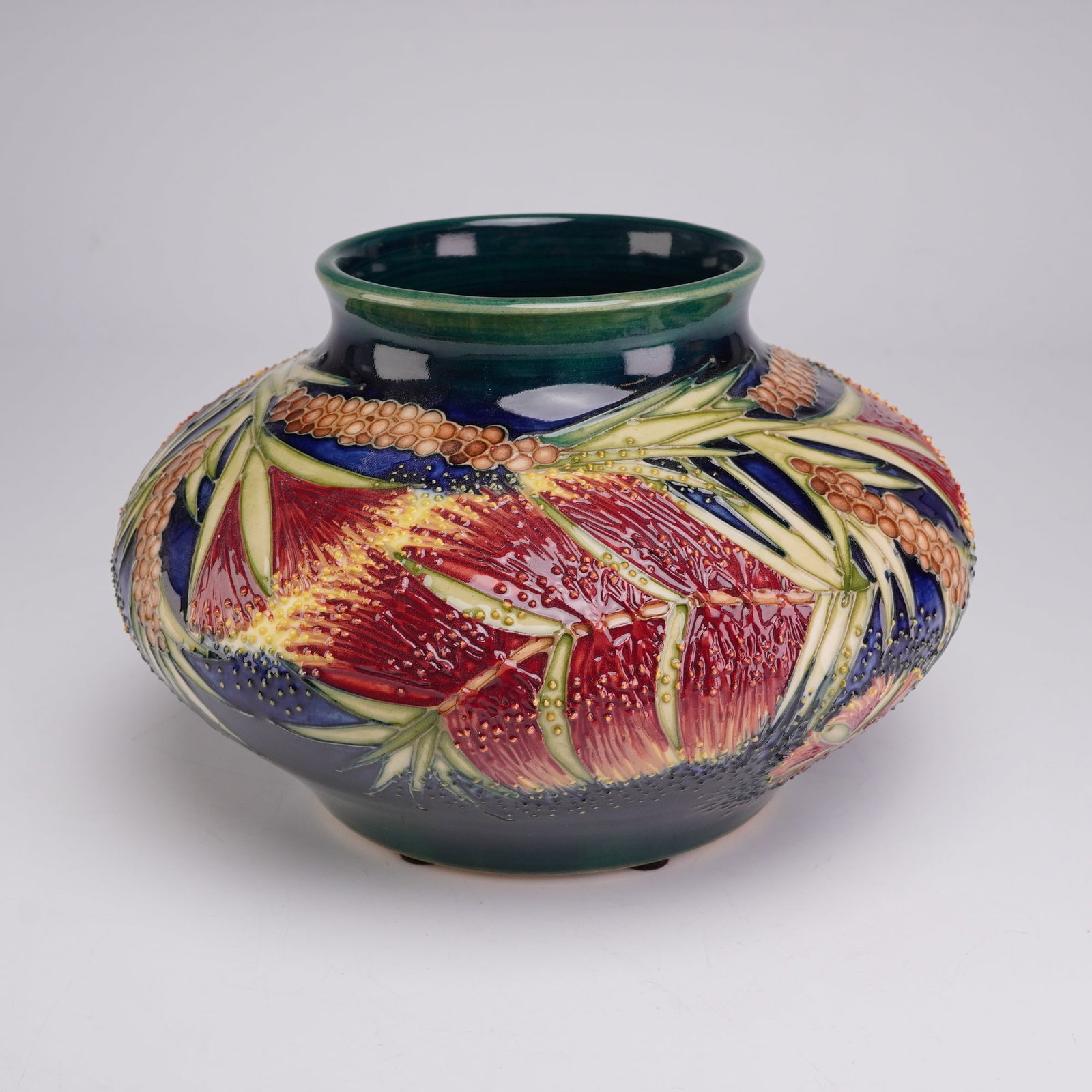 Moorcroft Pottery Limited Edition Vase, Malahide for James Macintyre and Co. Ltd.: The vessel features a squat, bulbous form with a short, wide neck and a slightly flared rim. The exterior is decorated with a vibrant botanical motif depicting red and yellow bottle brush blossoms amo