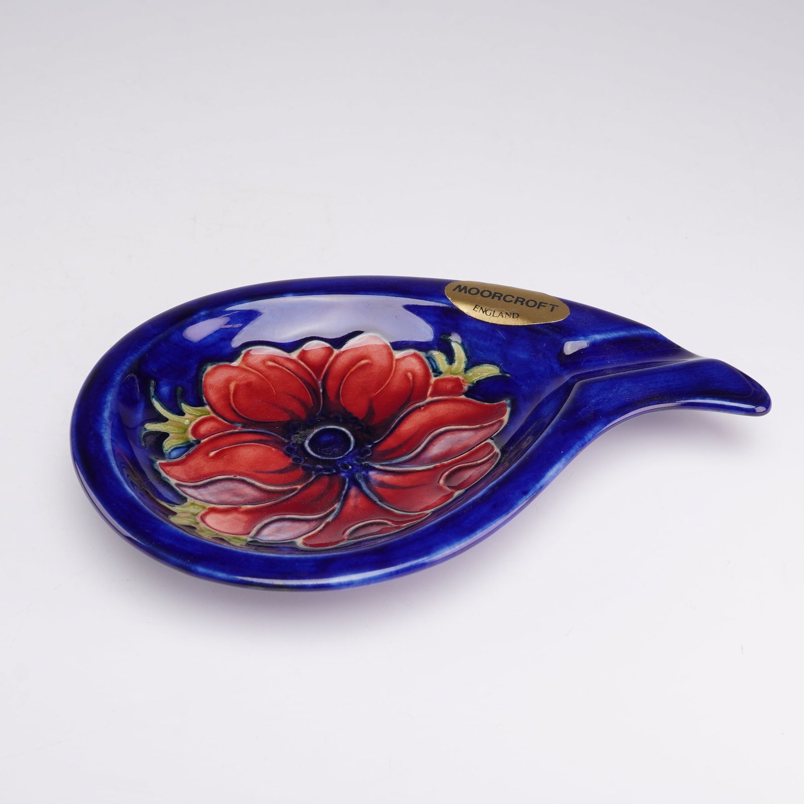 Moorcroft Pottery Ashtray, Anemone Pattern: A teardrop-shaped ceramic ashtray produced by Moorcroft in England. This piece features the hand-painted and tube-lined Anemone pattern, decorated with a central red and pink flower accented by green 