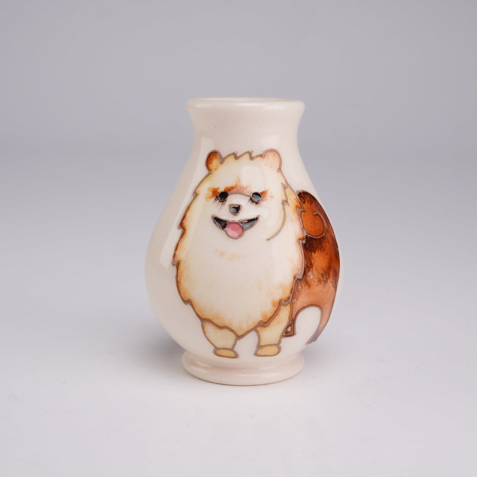 Moorcroft Miniature Dog Vase, Pomeranian: This is a hand-painted miniature ceramic bud vase produced by Moorcroft Pottery. The vessel features a bulbous body that tapers to a short neck with a slightly flared rim, resting on a small integrate
