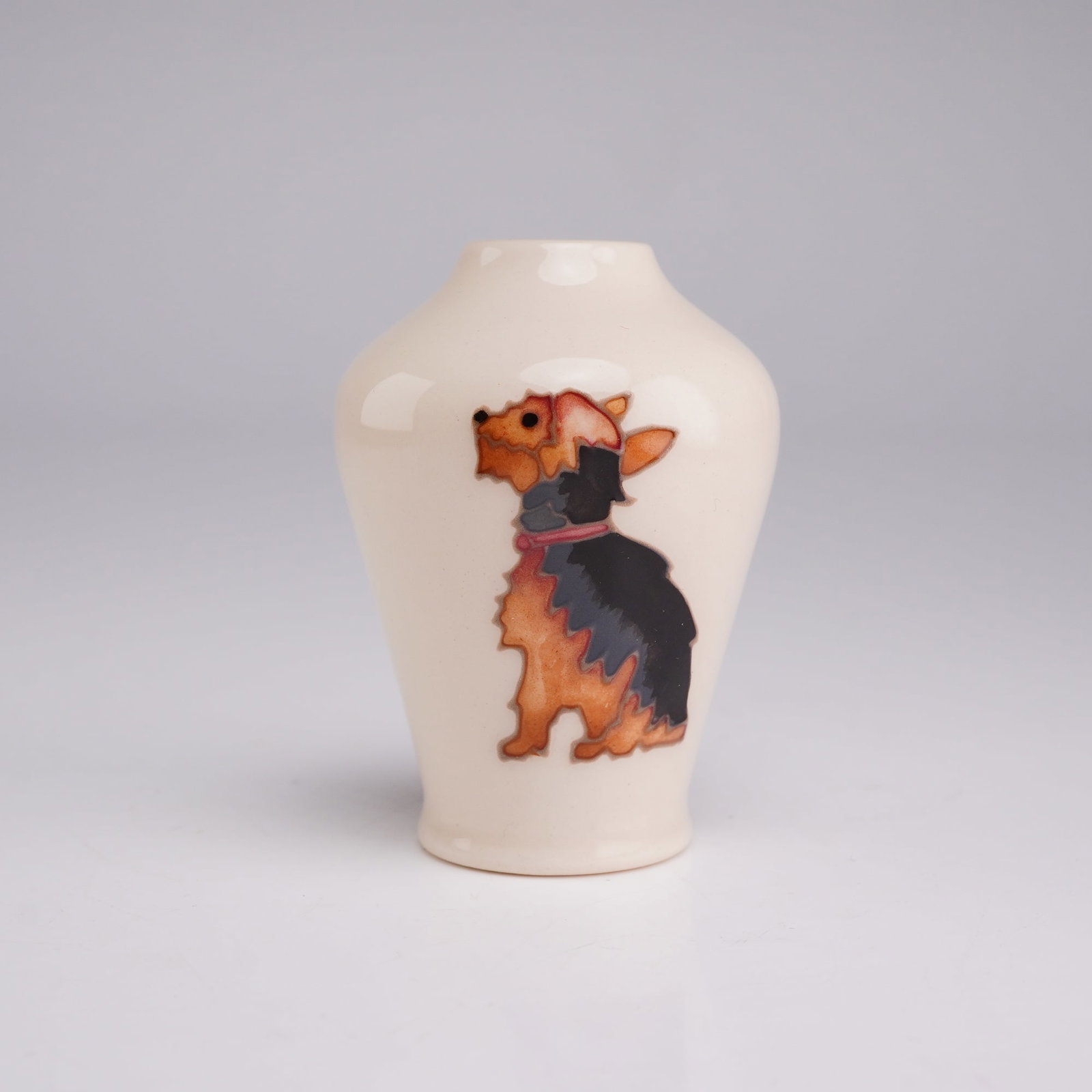 Moorcroft Pottery Miniature Dog Vase, Yorkshire Terrier: This miniature pottery bud vase features a baluster-shaped body with a narrow opening and a slightly flared foot. The vase is finished in a glossy cream-colored glaze and is decorated with a tubelined