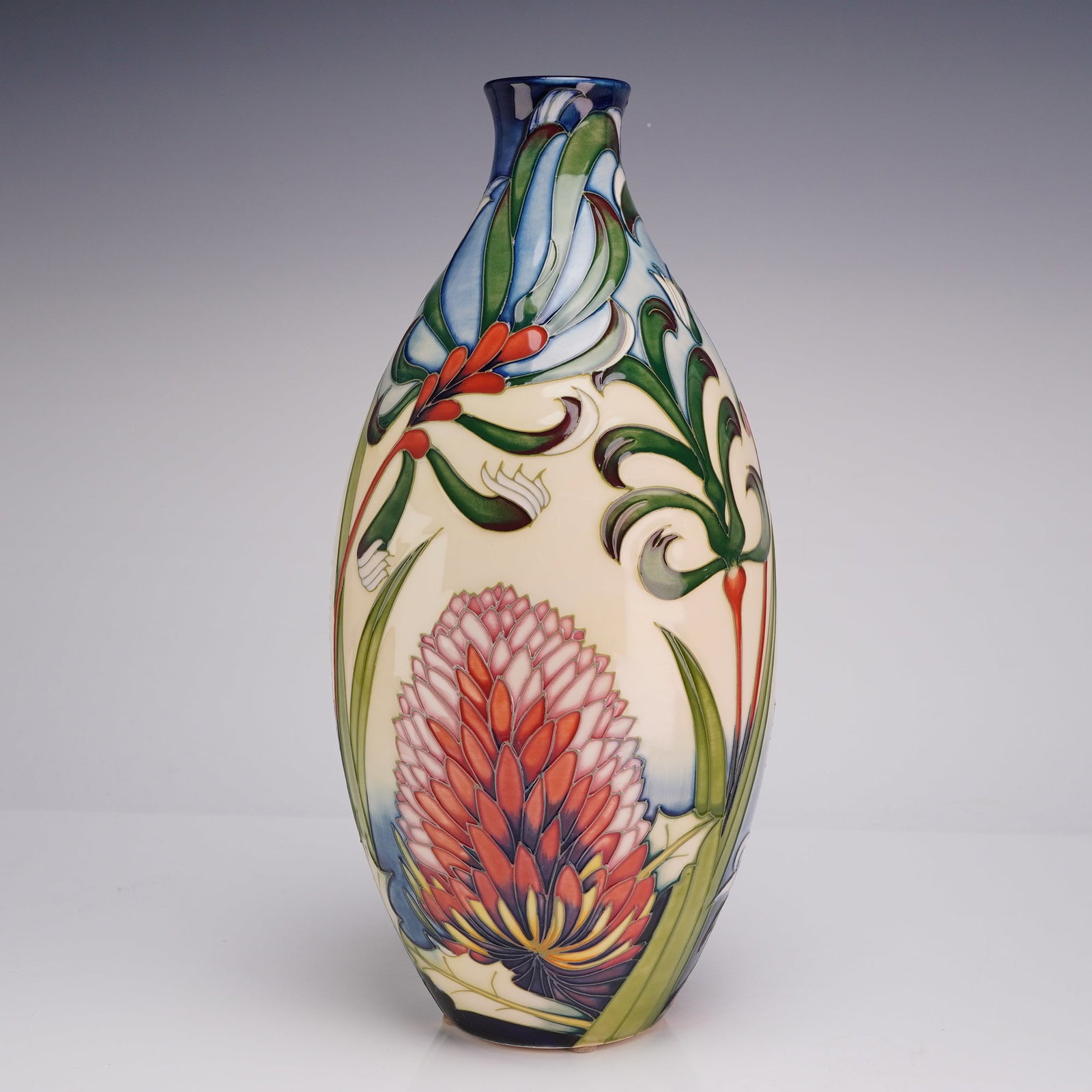 Moorcroft Art Pottery Australian Firewheel Banksia Vase: A Moorcroft art pottery earthenware vase of elongated ovoid form, tapering to a slender neck with a flared rim. The vessel is decorated in the Firewheel Banksia pattern, featuring tubelined motifs of 