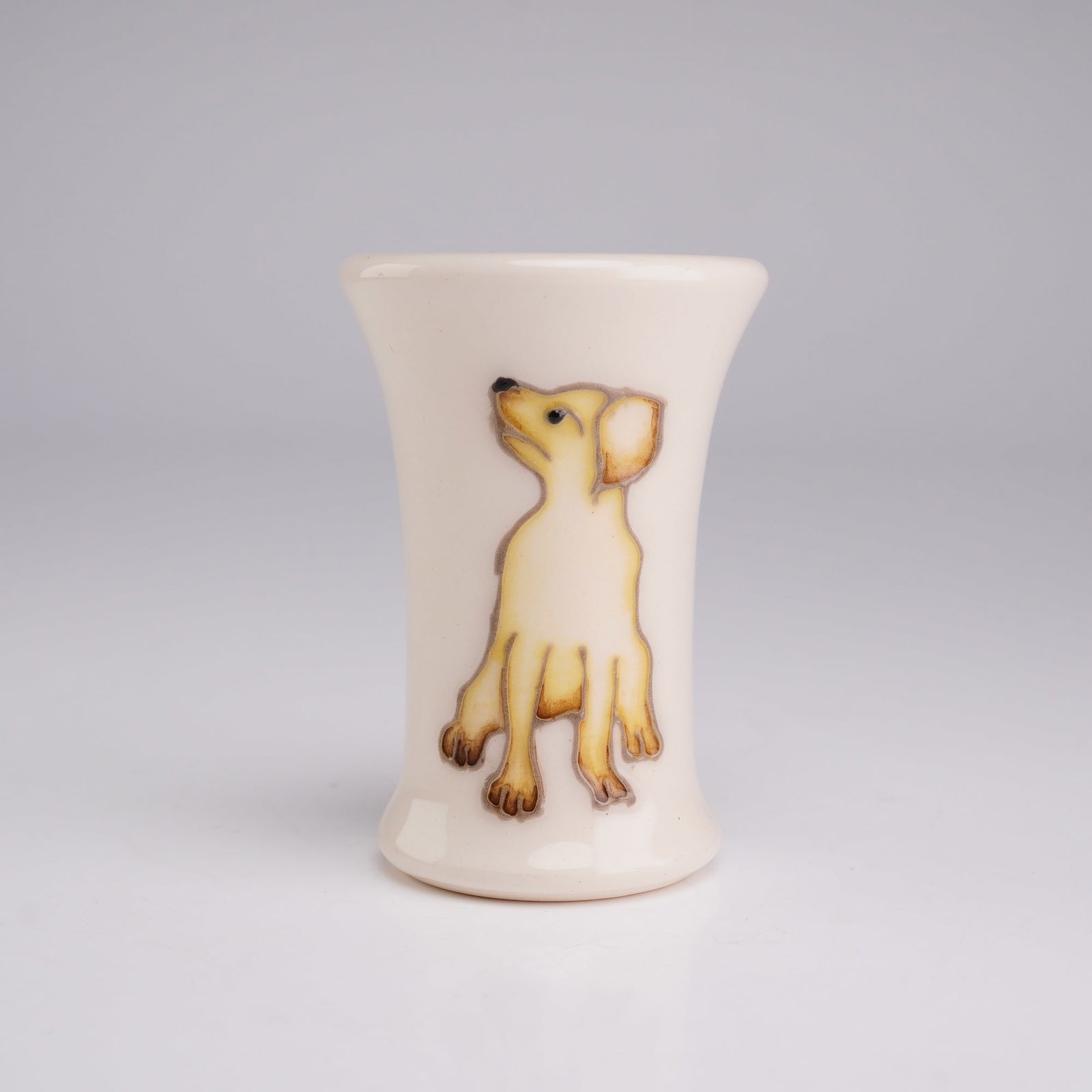 Moorcroft Pottery Miniature Puppy Vase, Yellow Labrador: The piece features a flared rim and a weighted, rounded base. It is decorated with a tube-lined and hand-painted design of a seated yellow Labrador retriever puppy against a cream ground. The undersid