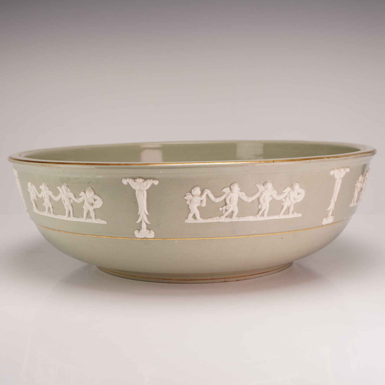 Wedgwood Glazed Celadon Green Jasperware Putti Serving Bowl: A mid-19th century glazed stoneware serving bowl manufactured by Wedgwood. The exterior features a pale celadon or seafoam green ground decorated with applied white jasperware-style sprigged reliefs. 