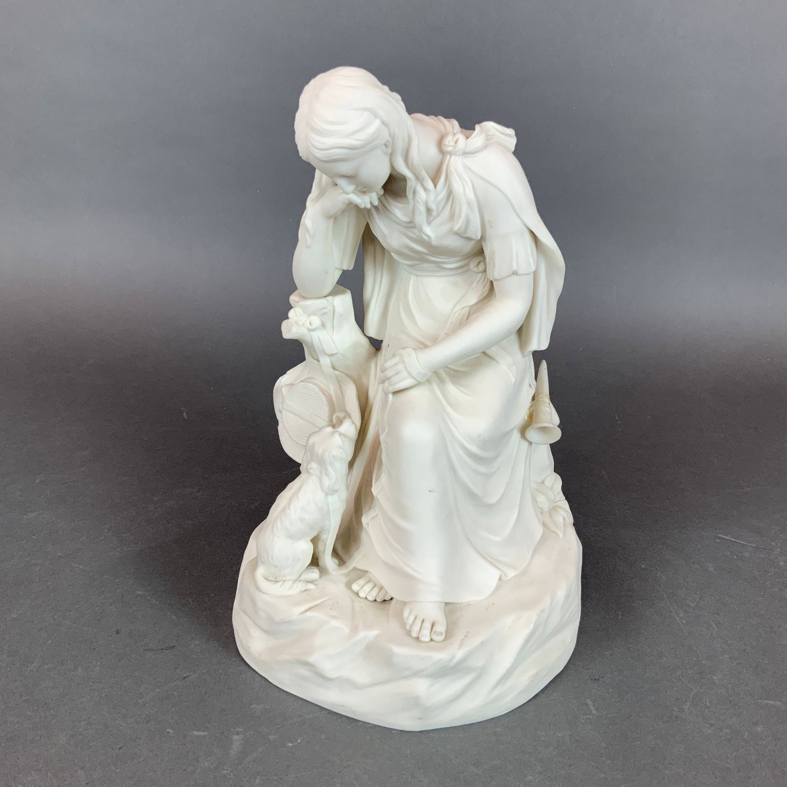 Wedgwood Neoclassical Style Bisque Porcelain Figural Group of a Seated Woman and Dog: A Wedgwood Neoclassical style figural group crafted from white bisque porcelain with a matte, unglazed finish. The sculpture depicts a draped female figure in a seated pose on a naturalistic rocky mou