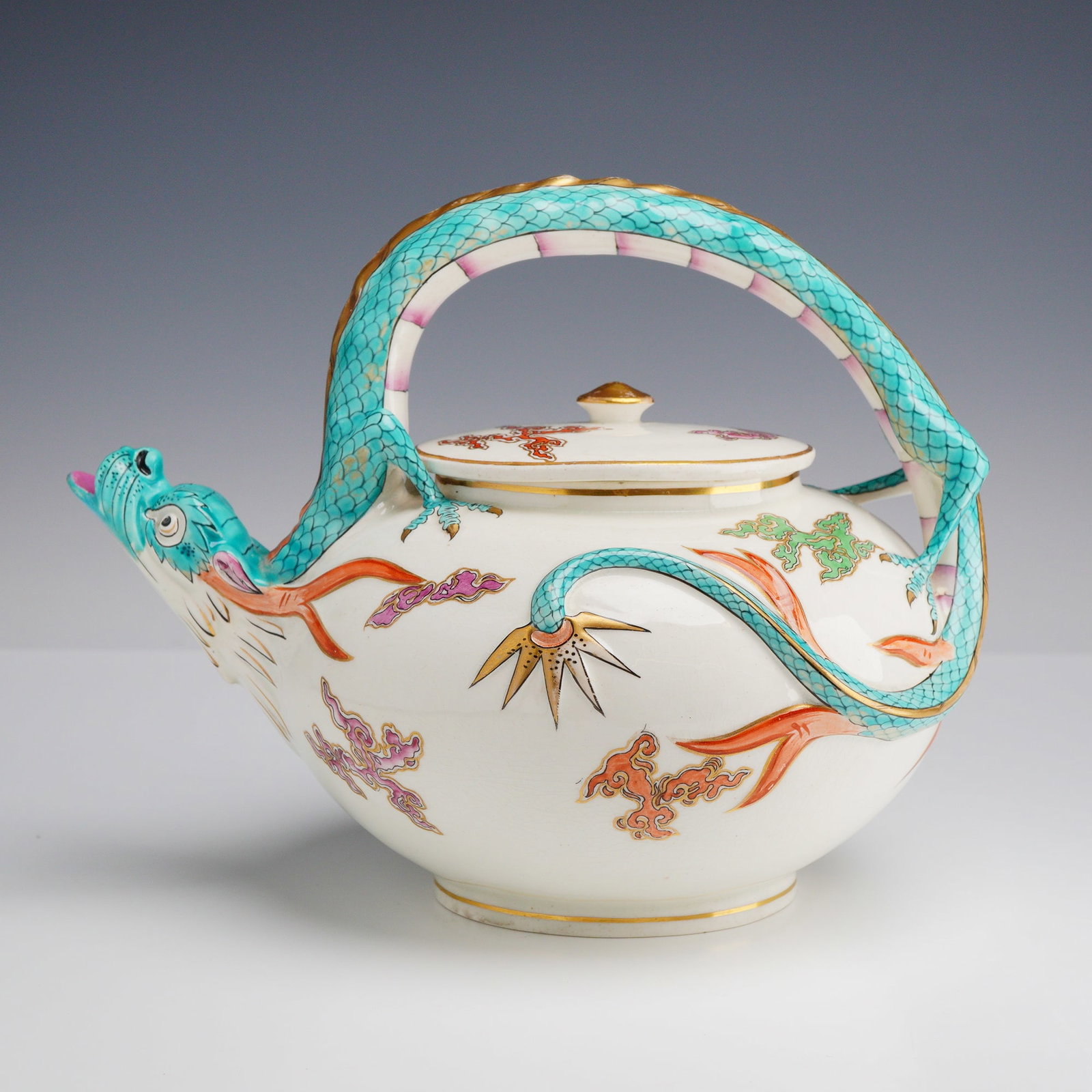 Wedgwood Chinoiserie Dragon Bridge Handle Teapot: This glazed white earthenware teapot by Wedgwood features a globular form with a distinctive bridge handle design. The spout is modeled as a dragon head with an open mouth, while the overhead handle i