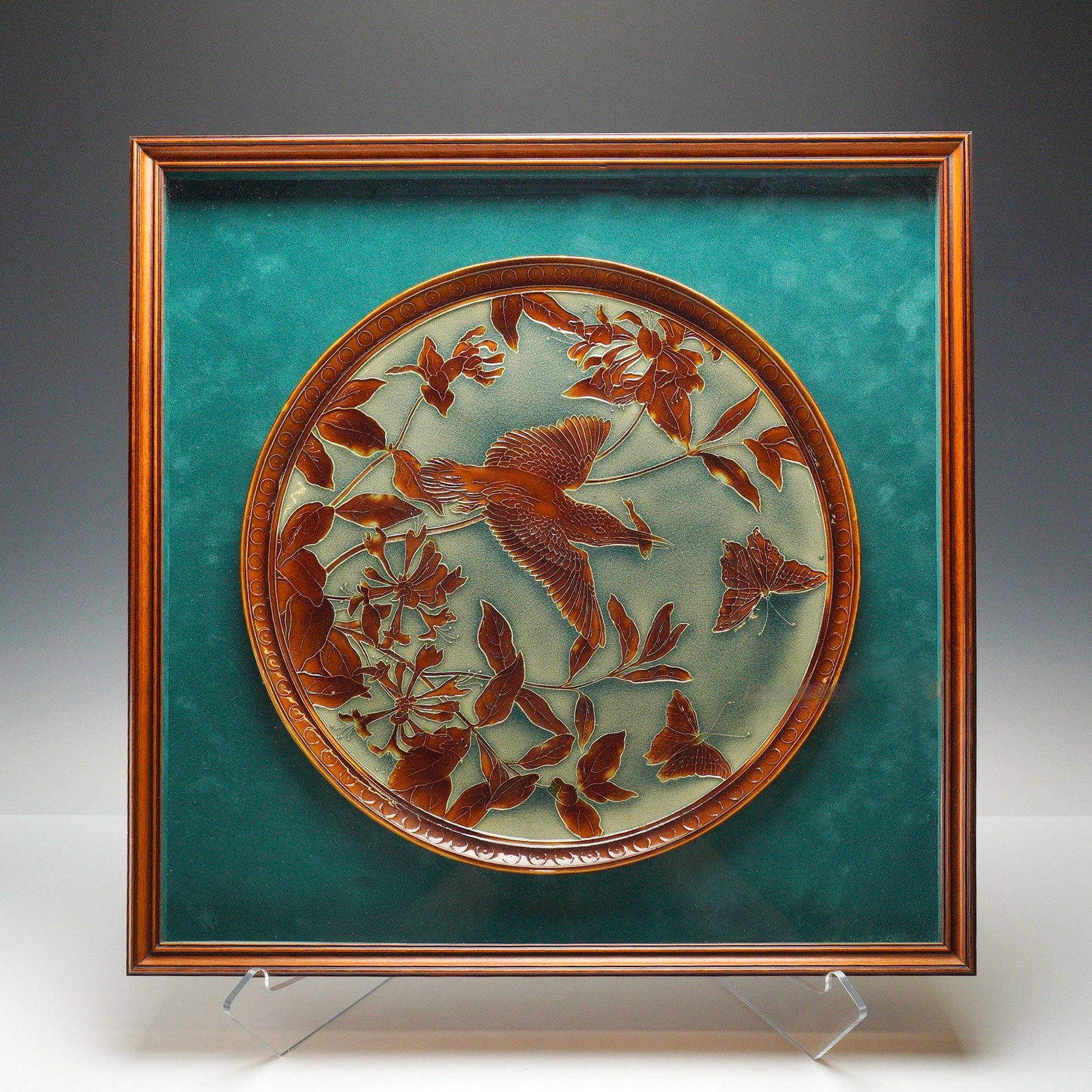 Framed Wedgwood Glazed Stoneware Bird and Butterflies Charger: A circular plate from Wedgwood featuring a bird and floral motif. The plaque is constructed of layered glass with a mottled amber and brown upper layer that has been acid-etched to create a raised rel