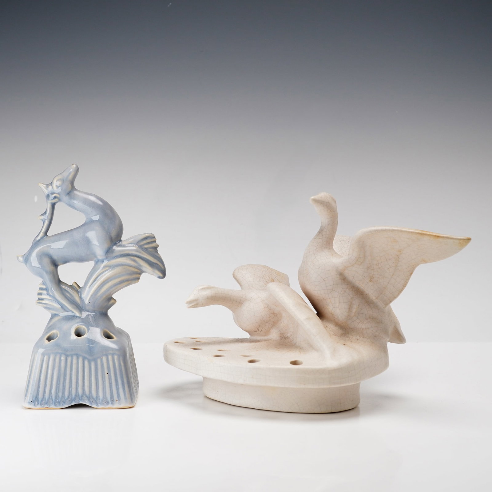 2pc American Art Pottery Flower Frogs w/ Hall China Deer & Weller Brighton Geese: This lot features two American art pottery flower frogs. The first is a blue-gray glazed earthenware piece featuring a stylized leaping deer or gazelle surmounting a square, pedestaled base with verti