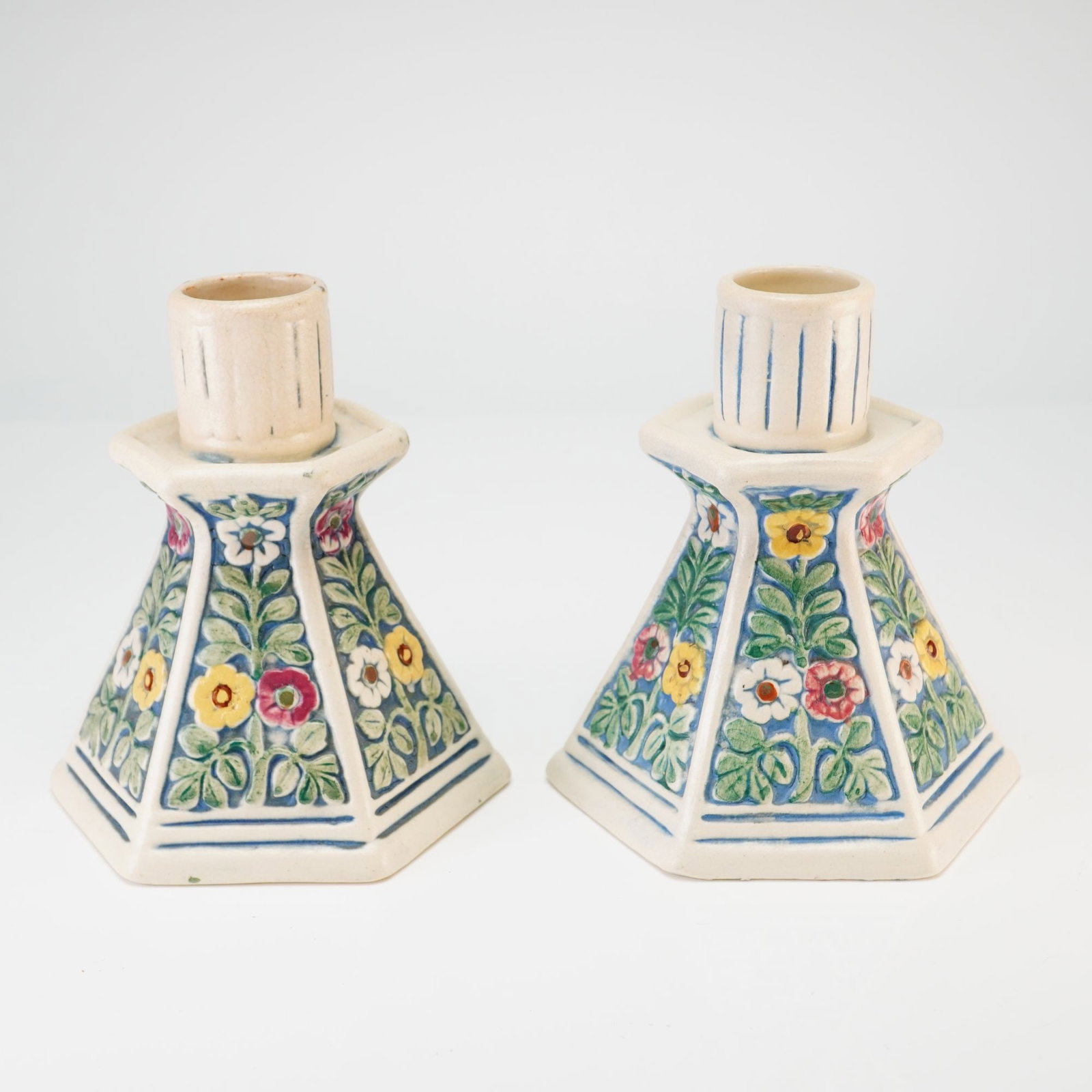 Pair of Weller Pottery Candlestick Holders, Florala Pattern: This pair of earthenware Weller candlesticks was produced by Weller Pottery of Zanesville, Ohio, in the Florala pattern, dating to the early 20th century, circa 1920. Each candlestick features a hexag