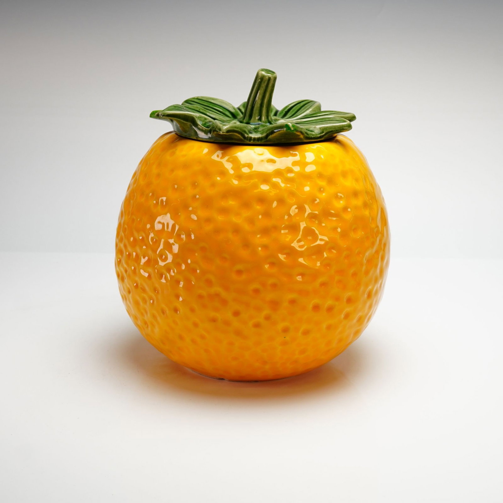 Vintage McCoy Pottery Lemon Cookie Jar Number 262 with Leaf Lid: A mid-20th-century American molded ceramic lidded cookie jar produced by McCoy Pottery. This whimsical kitchenware piece is designed in the form of a large lemon, featuring a globular earthenware body