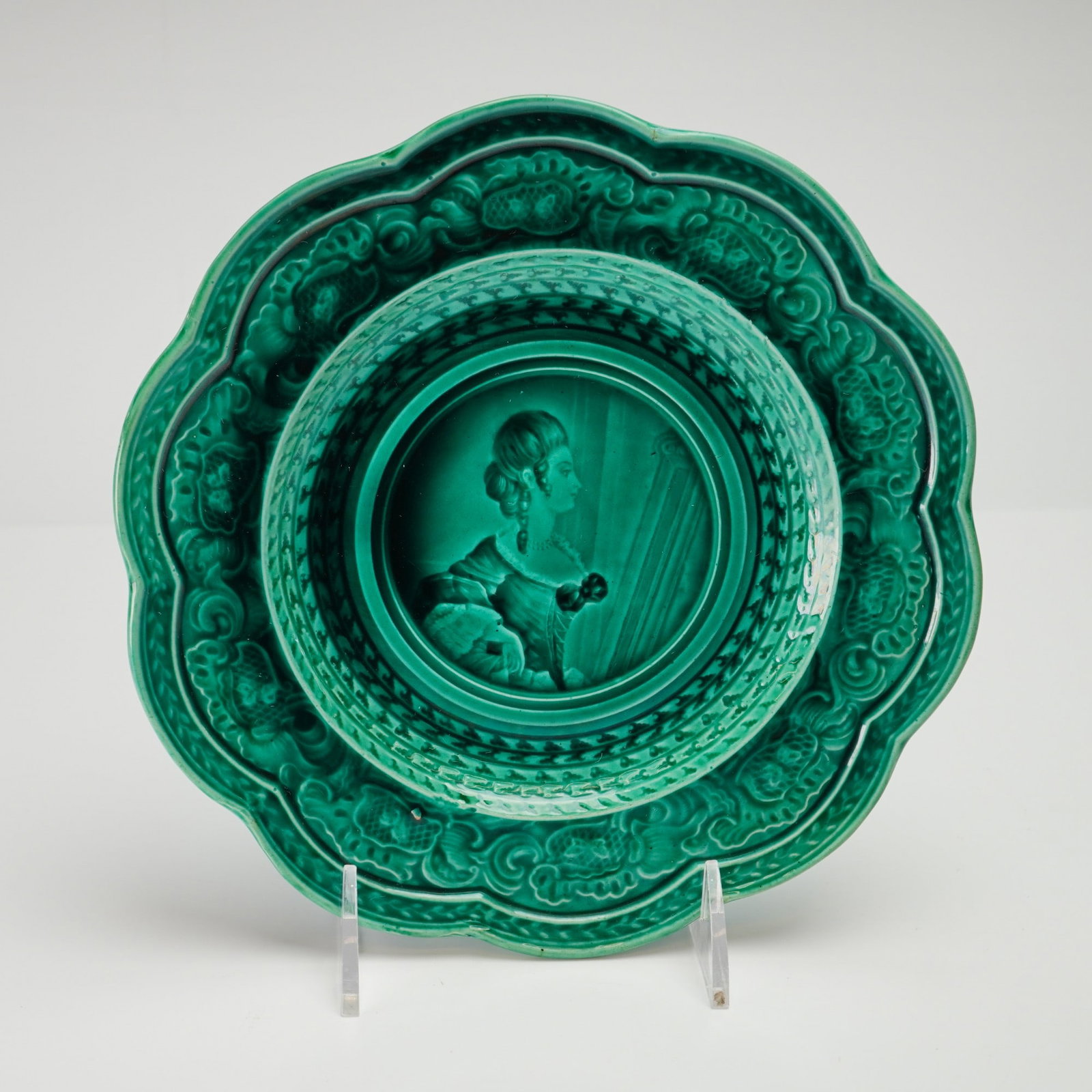 French Rubelles Emaux Ombrants Green Majolica Plate with Female Profile: This mid-19th century circular earthenware plate is a product of the Rubelles factory in France, featuring the emaux ombrants or shaded enamel technique. The plate is finished in a translucent emerald