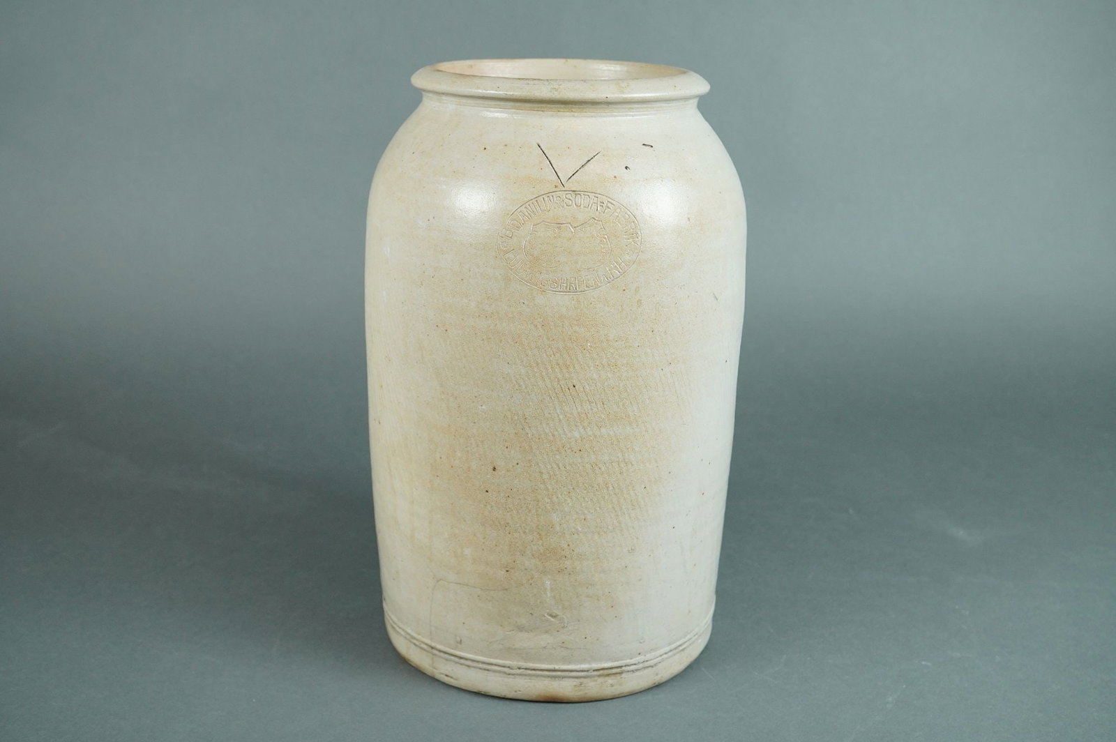 Badische Anilin & Soda-Fabrik Industrial Stoneware Storage Jar Ludwigshafen: A single antique utilitarian stoneware storage jar or crock featuring a cylindrical body, a short tapered neck, and a rolled rim. The vessel is covered in a mottled off-white salt glaze applied over a