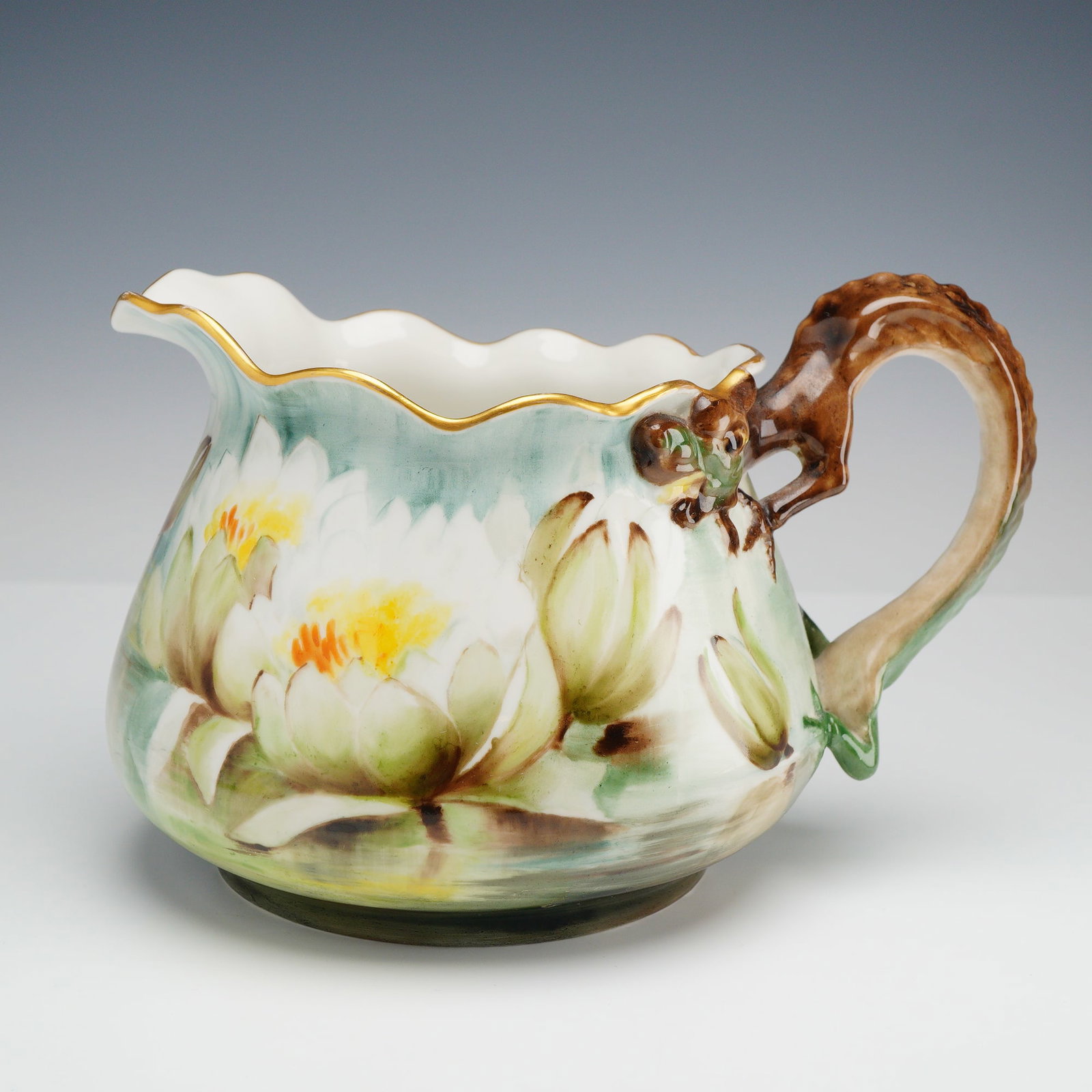 Jean Pouyat Limoges Hand-Painted Porcelain Water Lily Pitcher with Lizard Handle Signed Mrs.: A Jean Pouyat Limoges porcelain pitcher of squat, bulbous form featuring a ruffled rim with a gilded edge. The vessel is hand-painted with white water lilies and yellow centers amidst green pads on a 