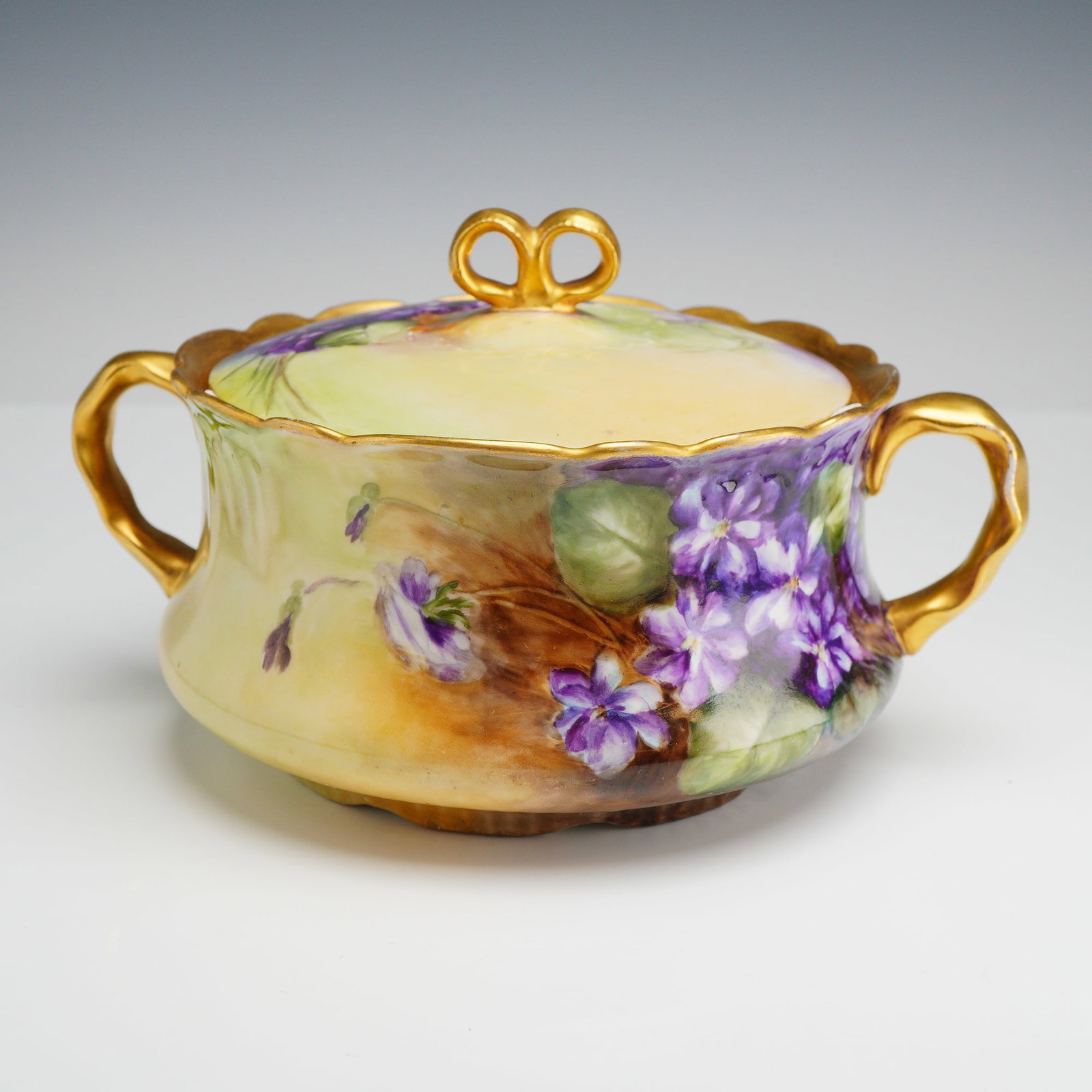 Jean Pouyat Limoges Hand-Painted Porcelain Lidded Pot: This hand-painted lidded porcelain pot was manufactured by the Jean Pouyat factory in Limoges, France. The vessel features a squat, bulbous body with a flaring, scalloped rim and two gilded, ear-shape