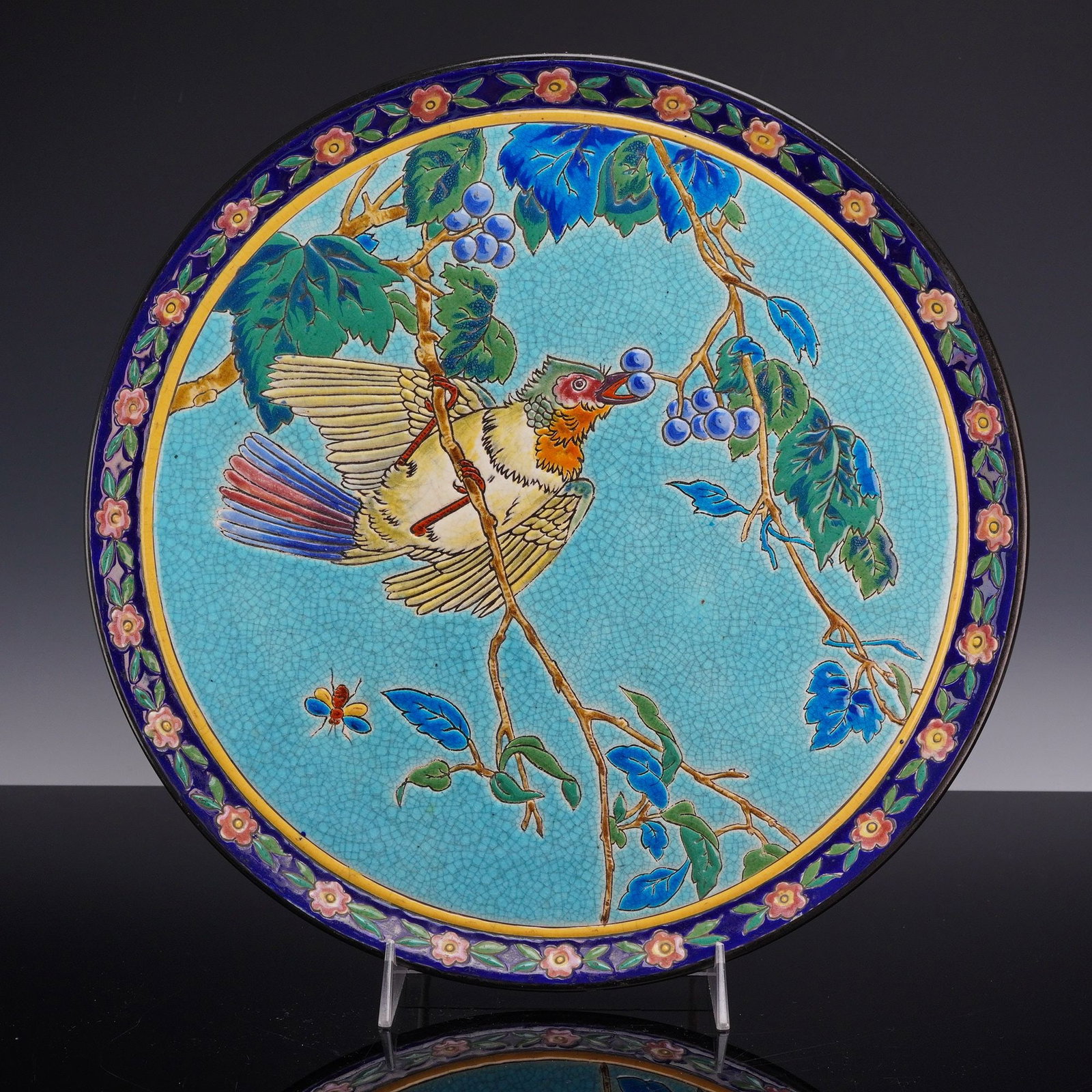 Emaux de Longwy Ceramic Platter with Bird Motif: This ceramic platter is a product of the Emaux de Longwy manufactory in France, featuring the signature emaux cernes technique. The piece is constructed from glazed earthenware (faience) with the deco