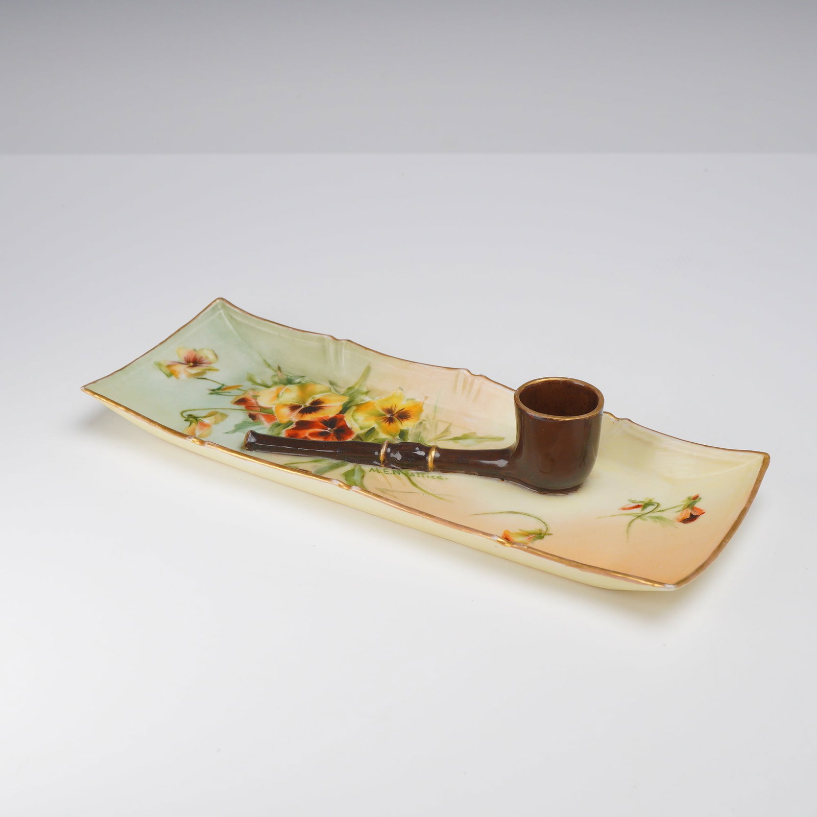 AK CD French Hand Painted Porcelain Pipe Rest Ashtray Signed M.E. Nattice: This French porcelain pipe rest ashtray features a rectangular form with a relief-molded, integrated sculptural pipe. The piece was produced by the firm of A. Klingenberg and Charles Dwenger (AK CD) o