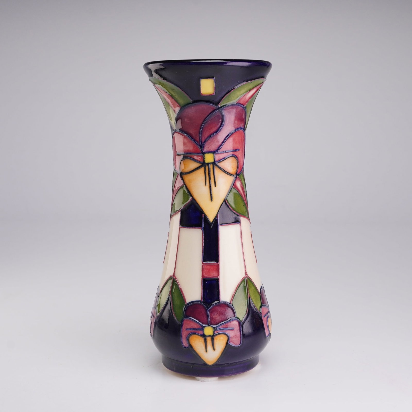 Moorcroft Pottery by Rachel Bishop Bud Vase, Trilogy: The decoration is executed using the tubelining technique, creating raised outlines that are hand-painted with glazes in shades of purple, pink, orange, yellow, and green. The floral motifs are set